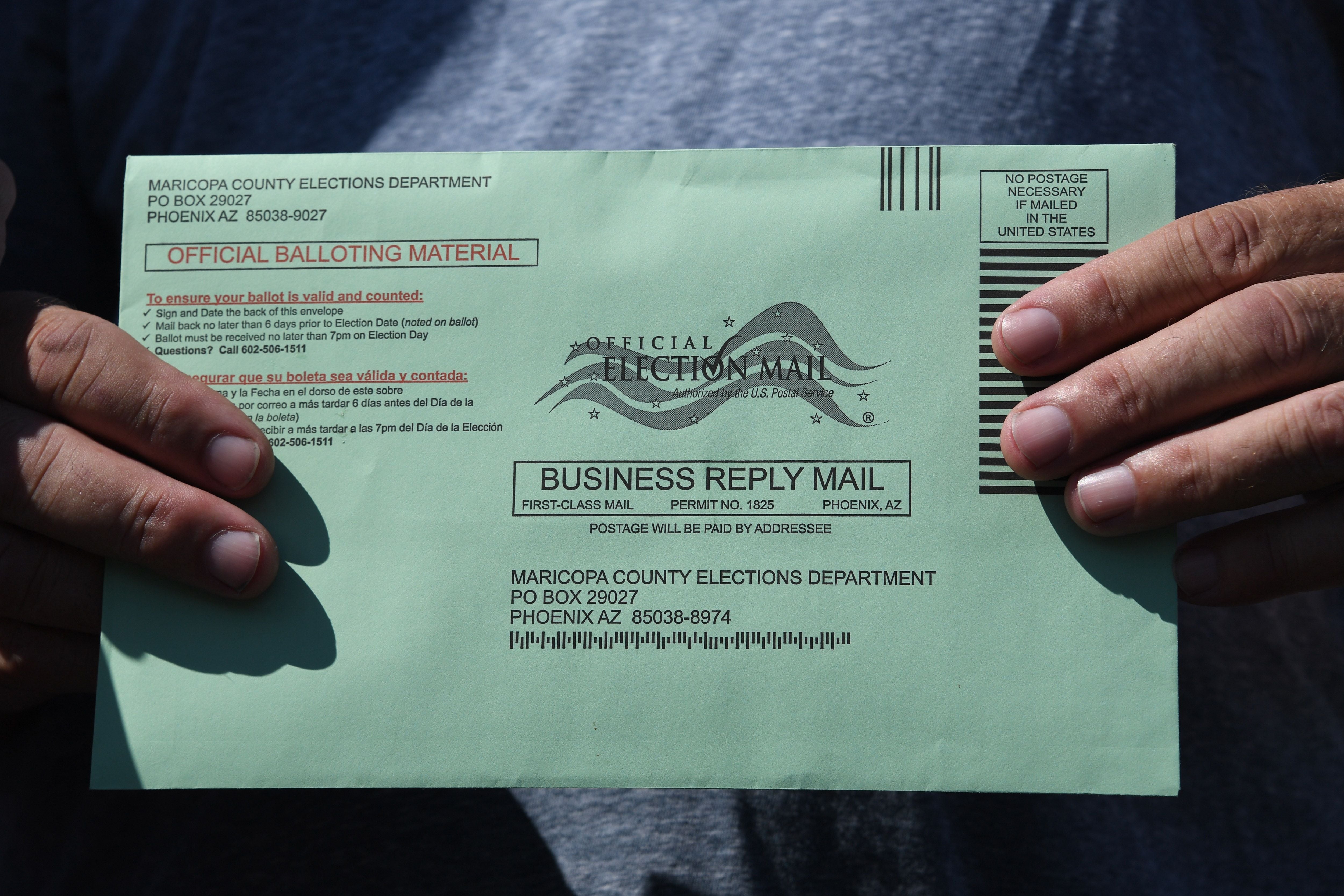 A closeup of someone’s hands holding a green envelope addressed to the Maricopa County Elections Department.