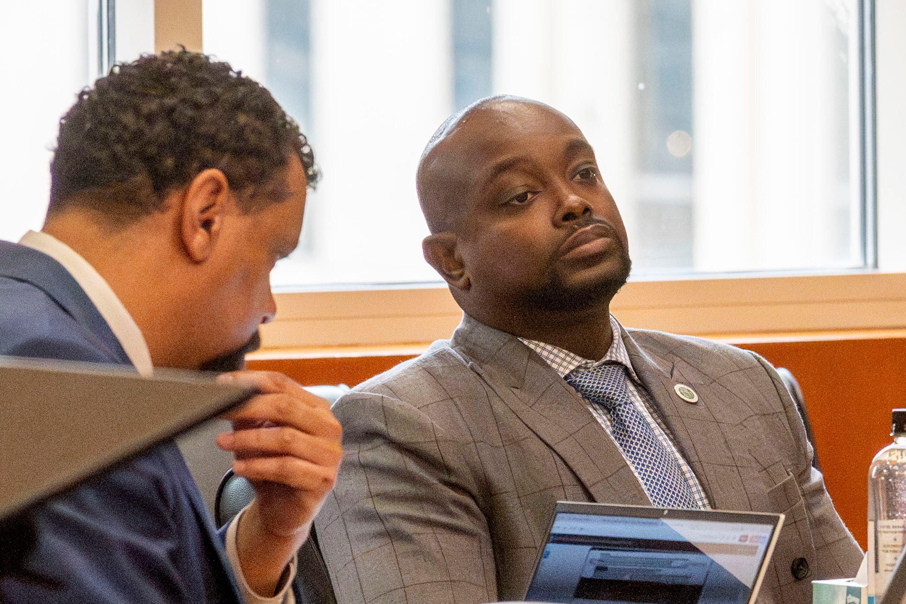 Two men in suits sit next to each other in a courtroom.