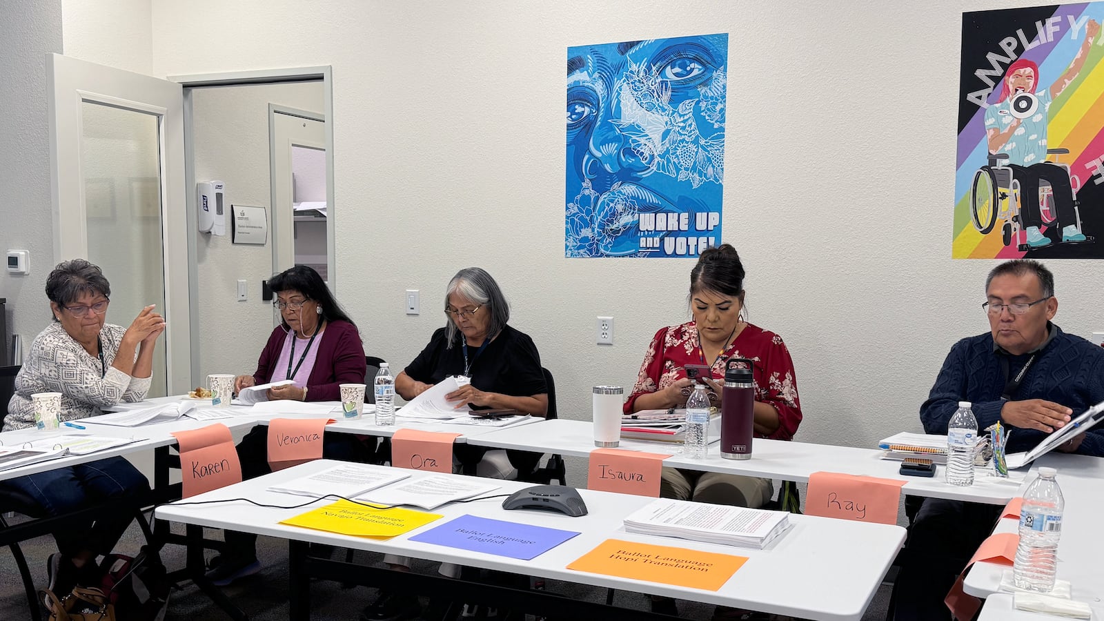 Five people sit behind a folding table with colorful signs around them.
