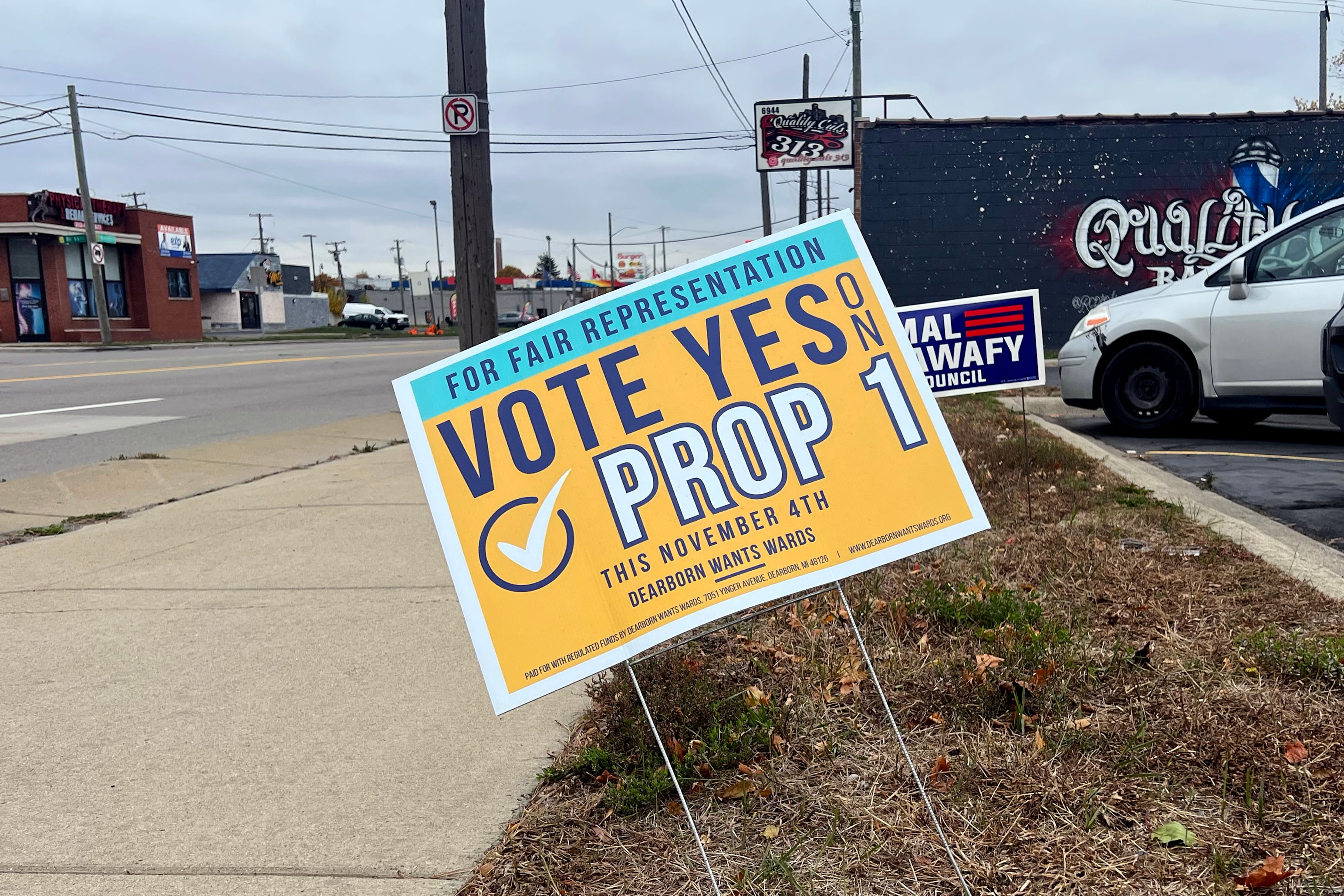 A photograph of a yellow political sign on a sidewalk outside with a grey sky in the background.