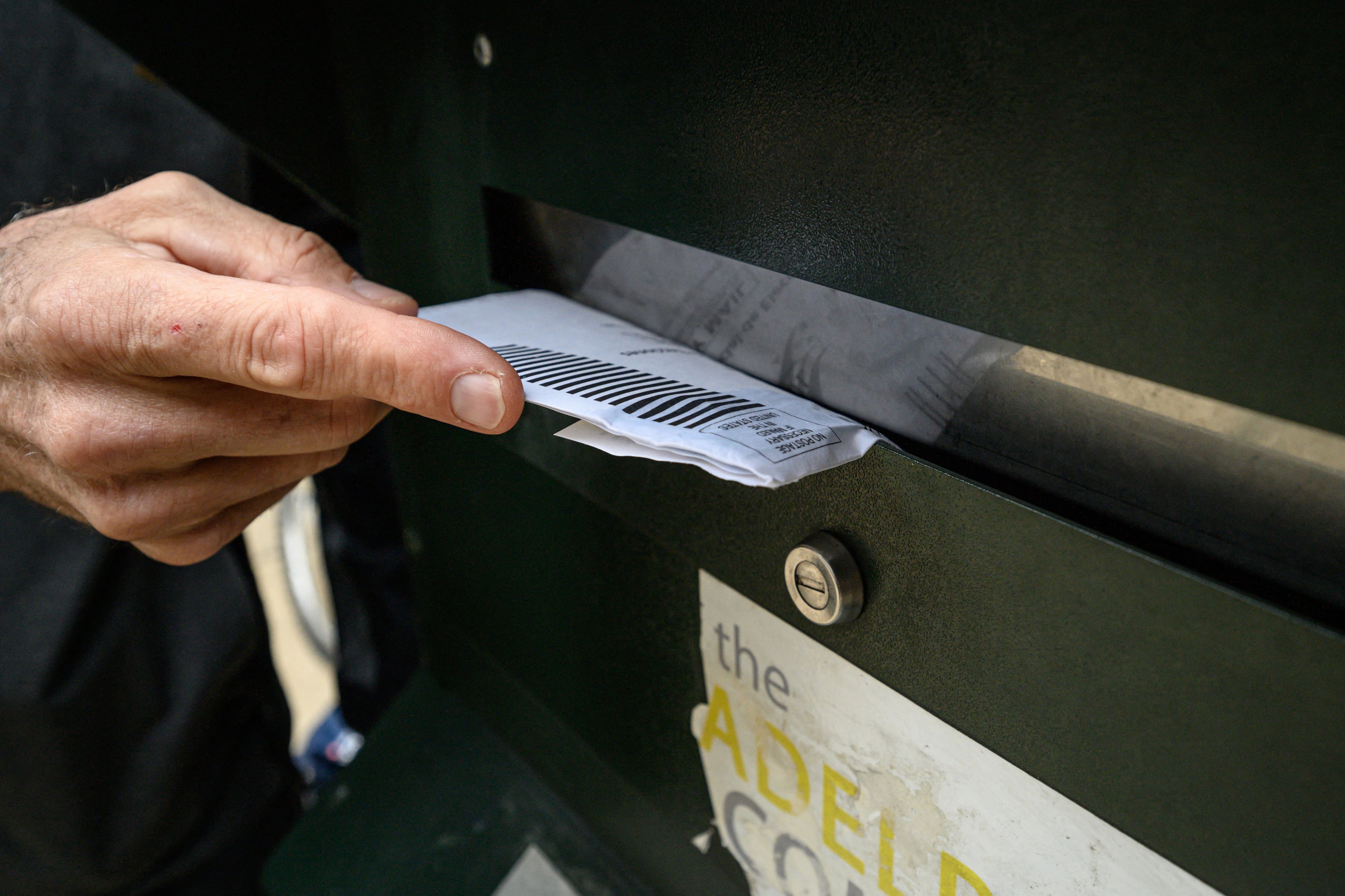 A close up of a hand placing a mail in ballot into a ballot box.