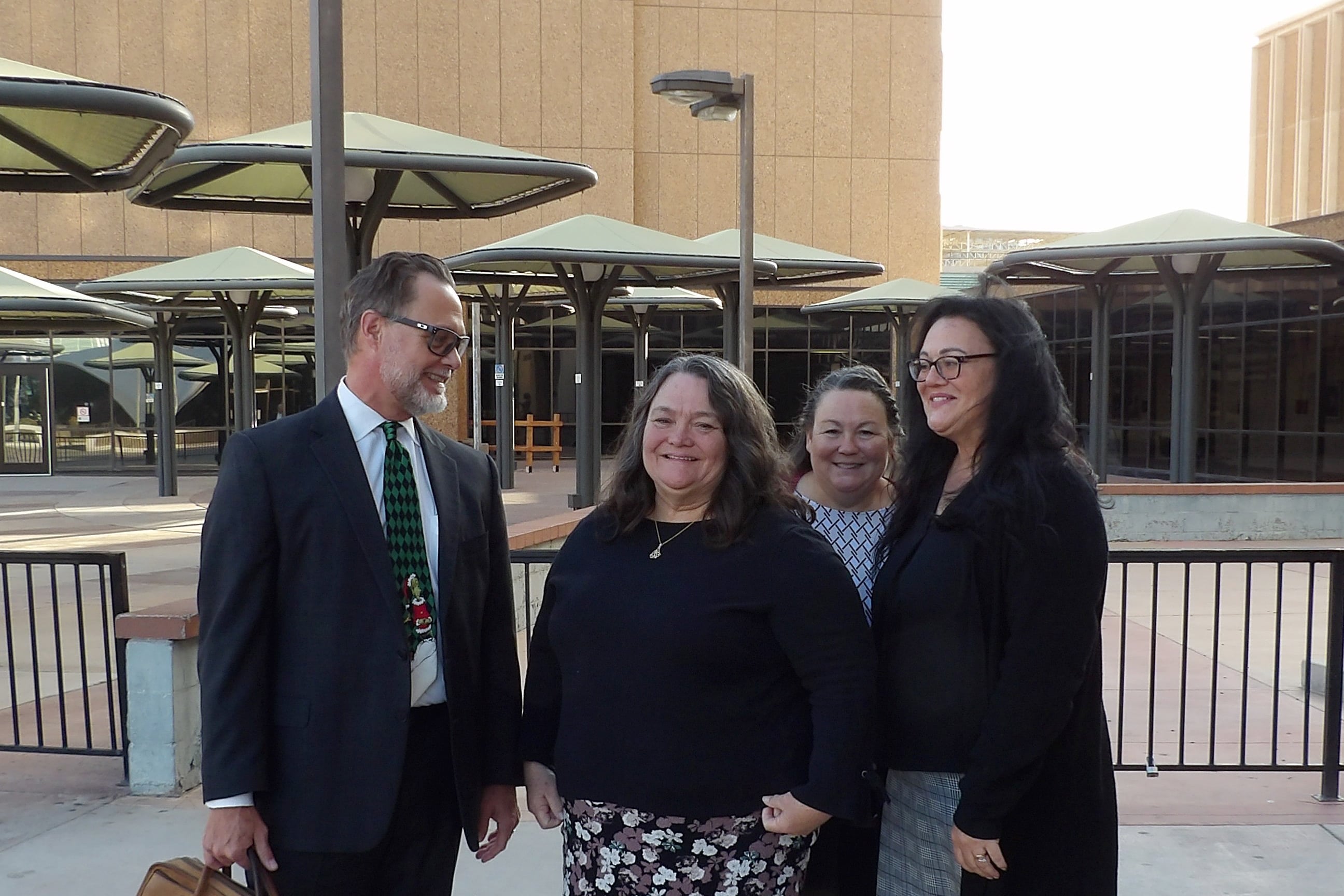 Four adults stand next to each other while standing outside with a building in the background.