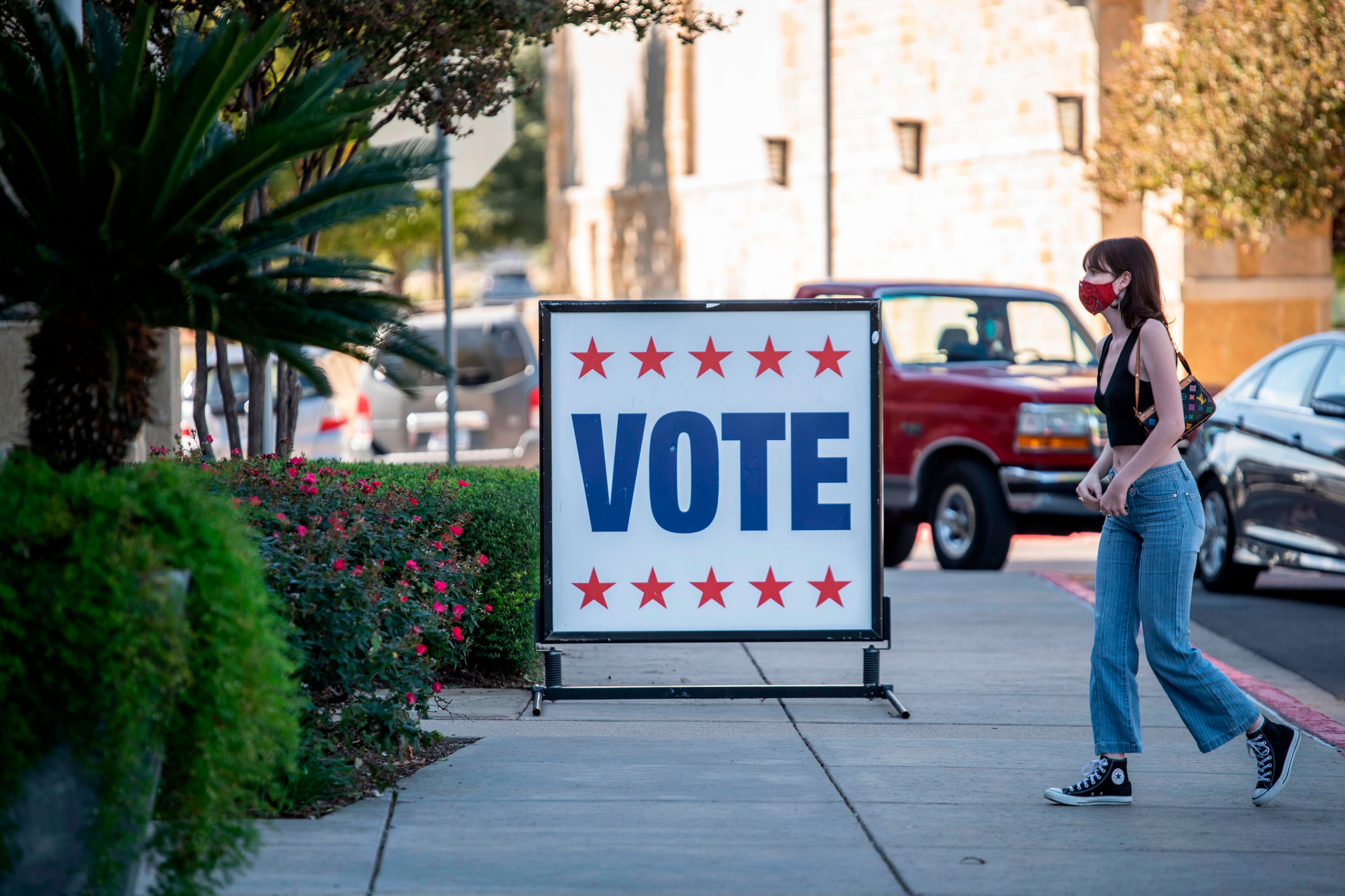 A young woman walks toward a building with a sign reading Vote in large letters.