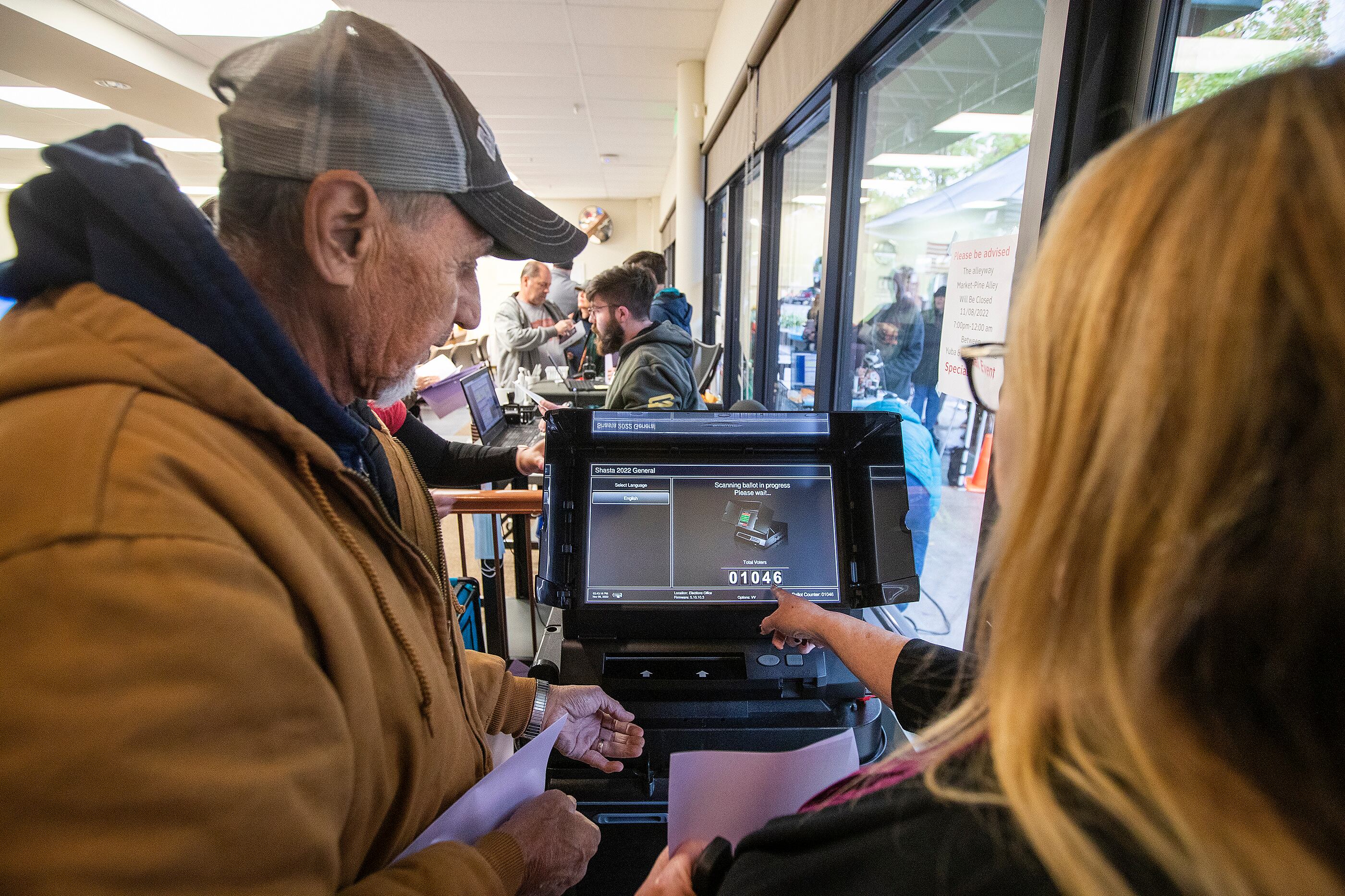 A woman points at the screen of a voting machine while a man looks on.