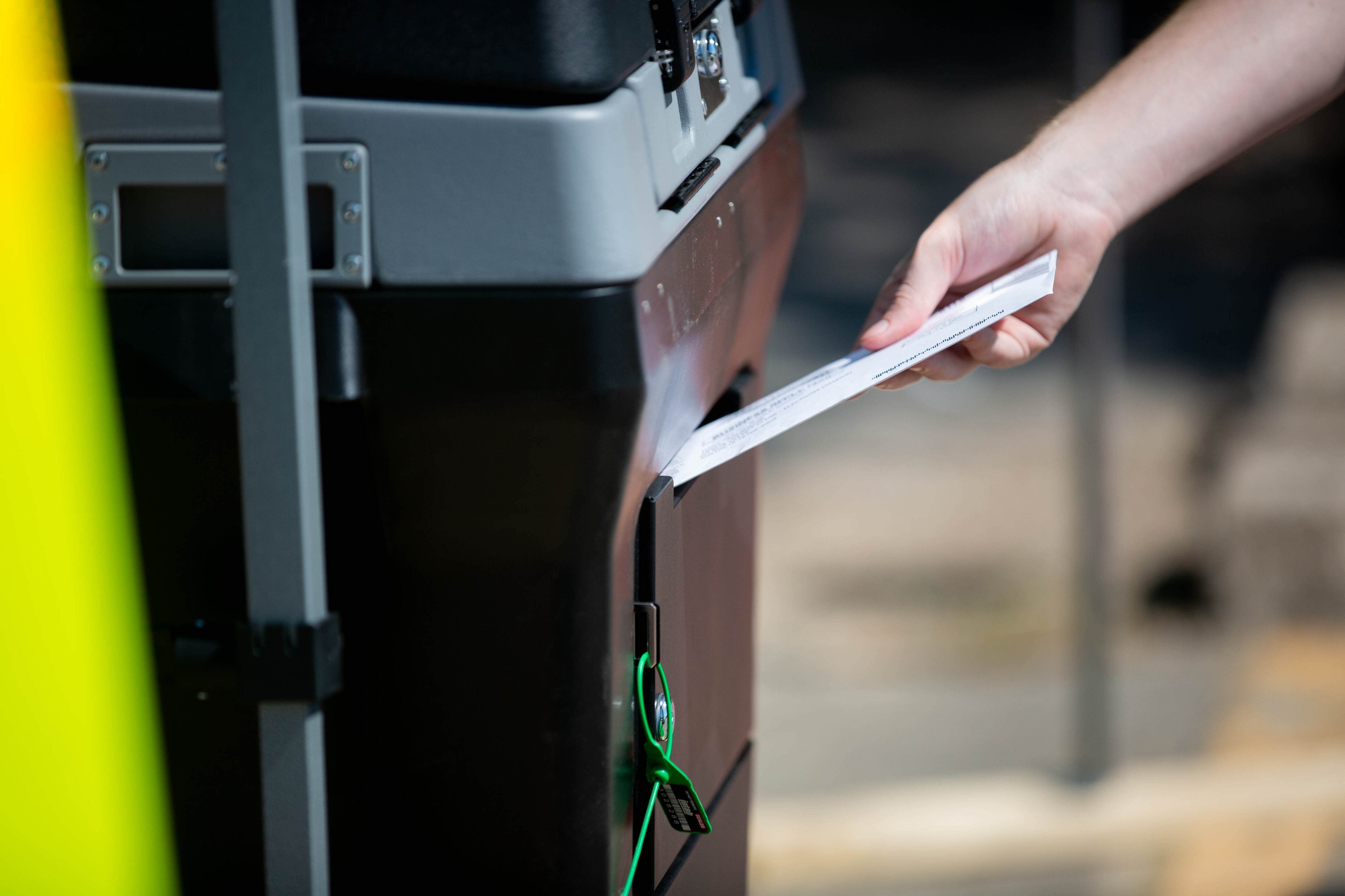 A person’s hand is shown holding an envelope and dropping it into a mail box