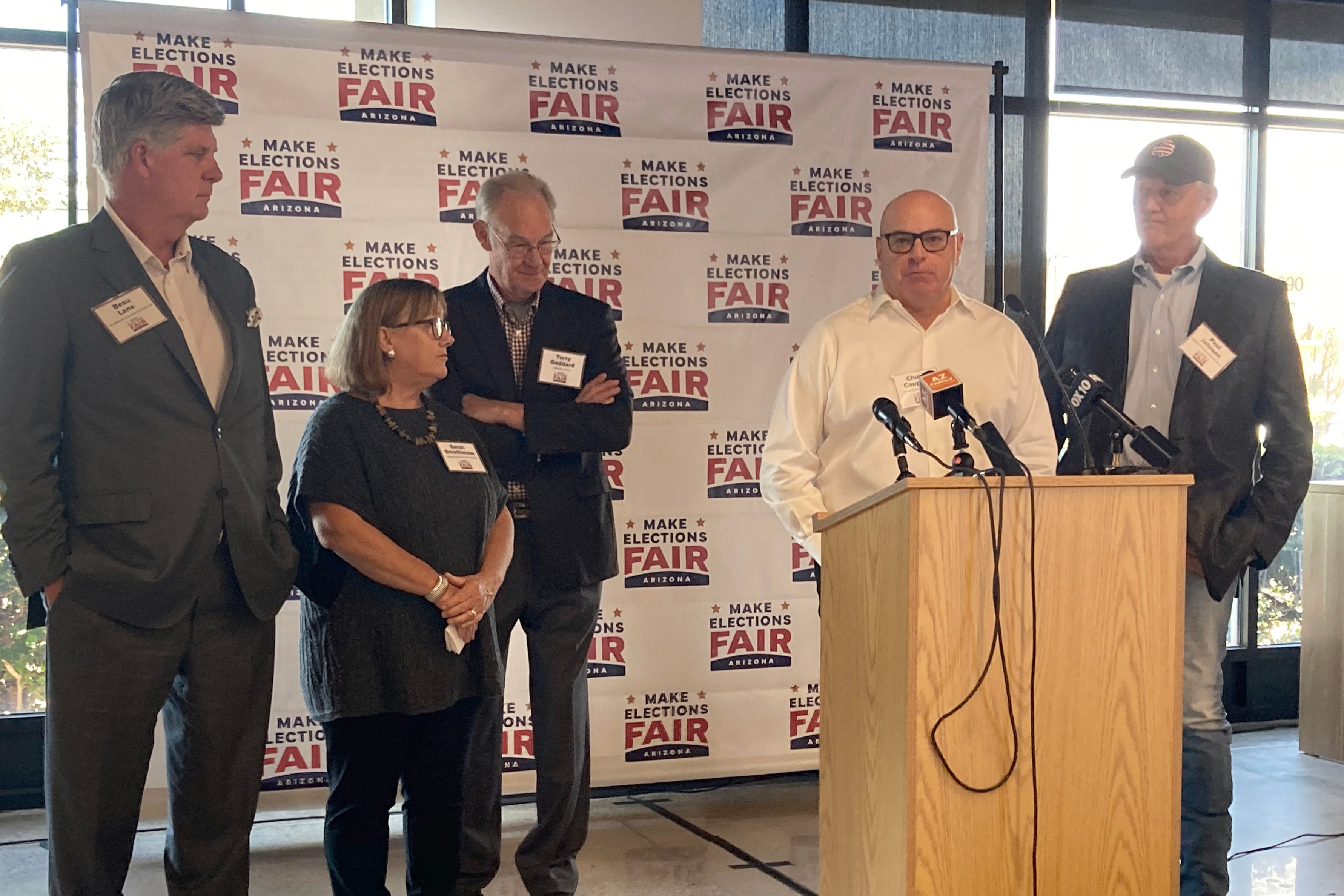 Five people stand behind a wooden podium and in front of a Make Elections Fair poster.