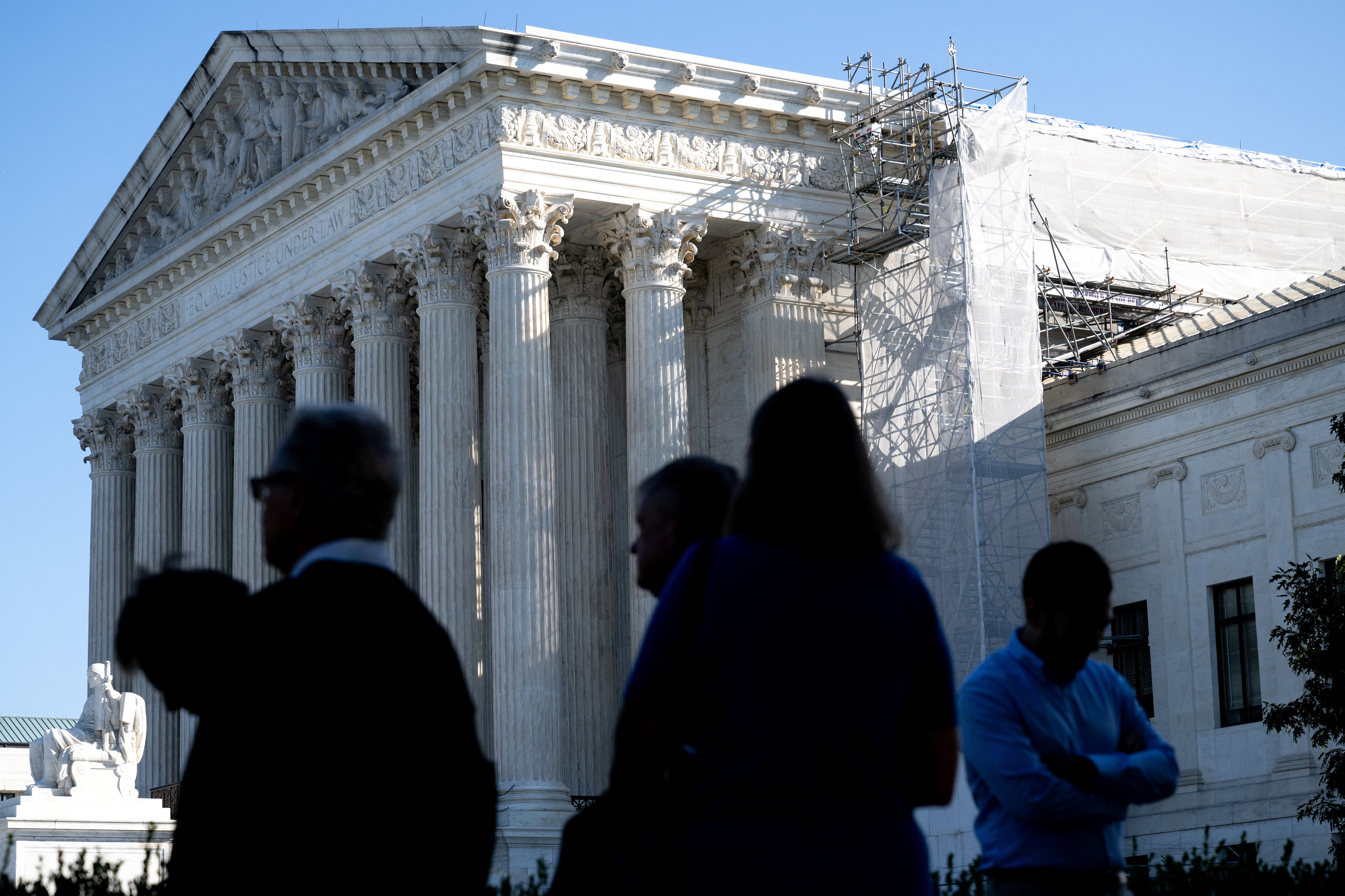 A group of people stand in the foreground out of focus while the front of the U.S. Supreme Court is visible.
