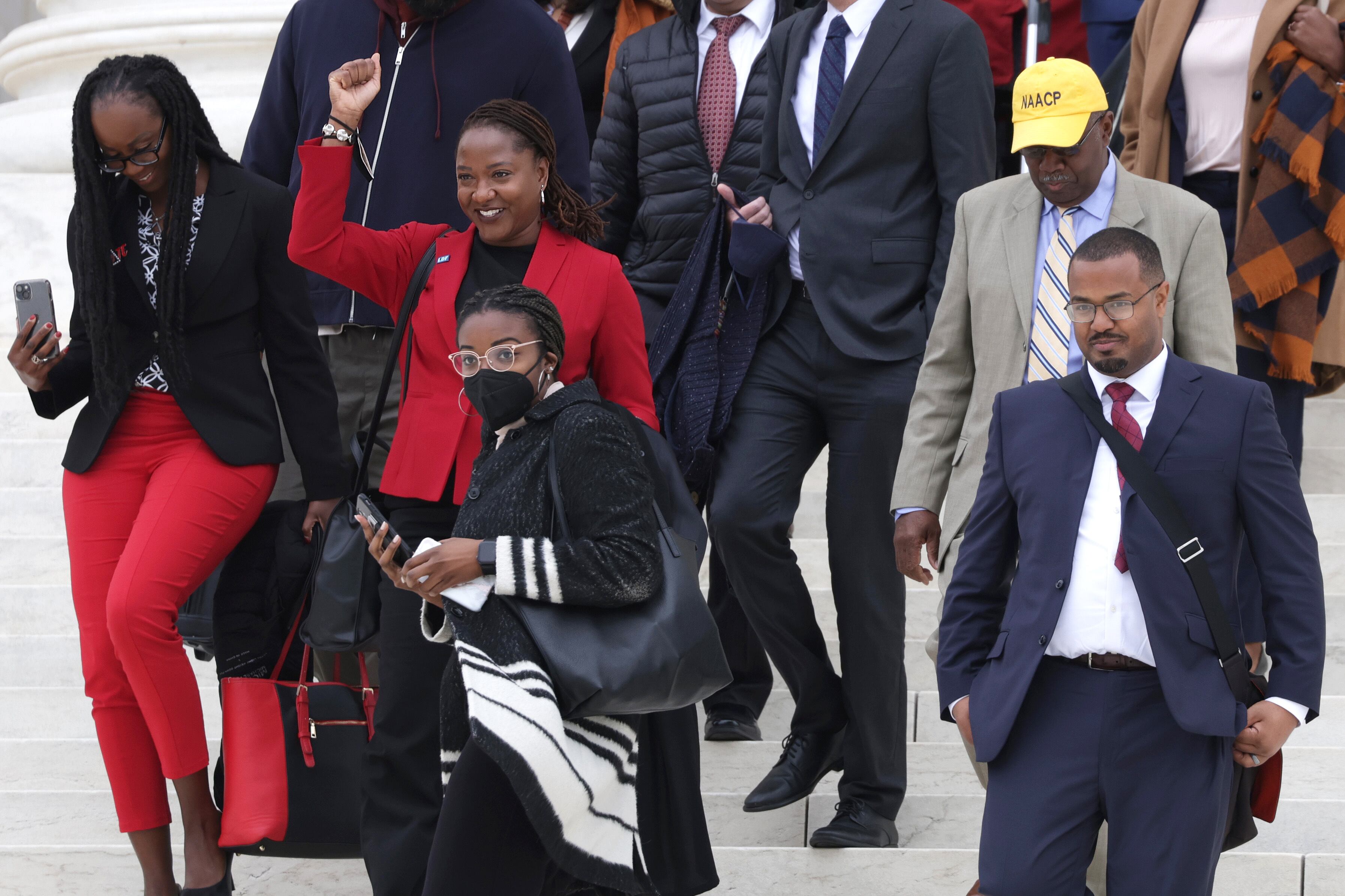 A woman in a red suit holds up her fist as she walks surrounded by other people.