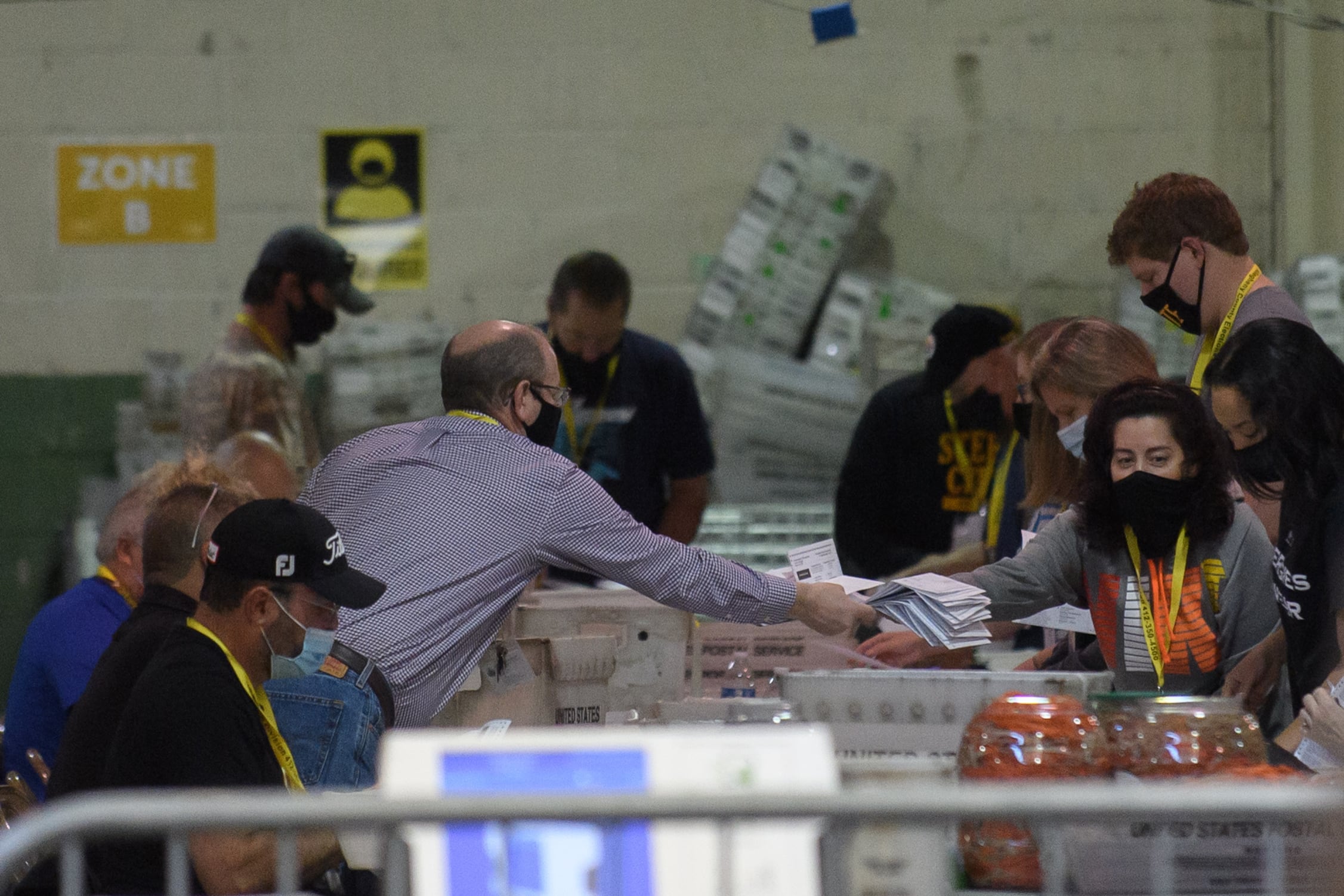 A group of people reach over a large, cluttered table, passing ballots to each other.