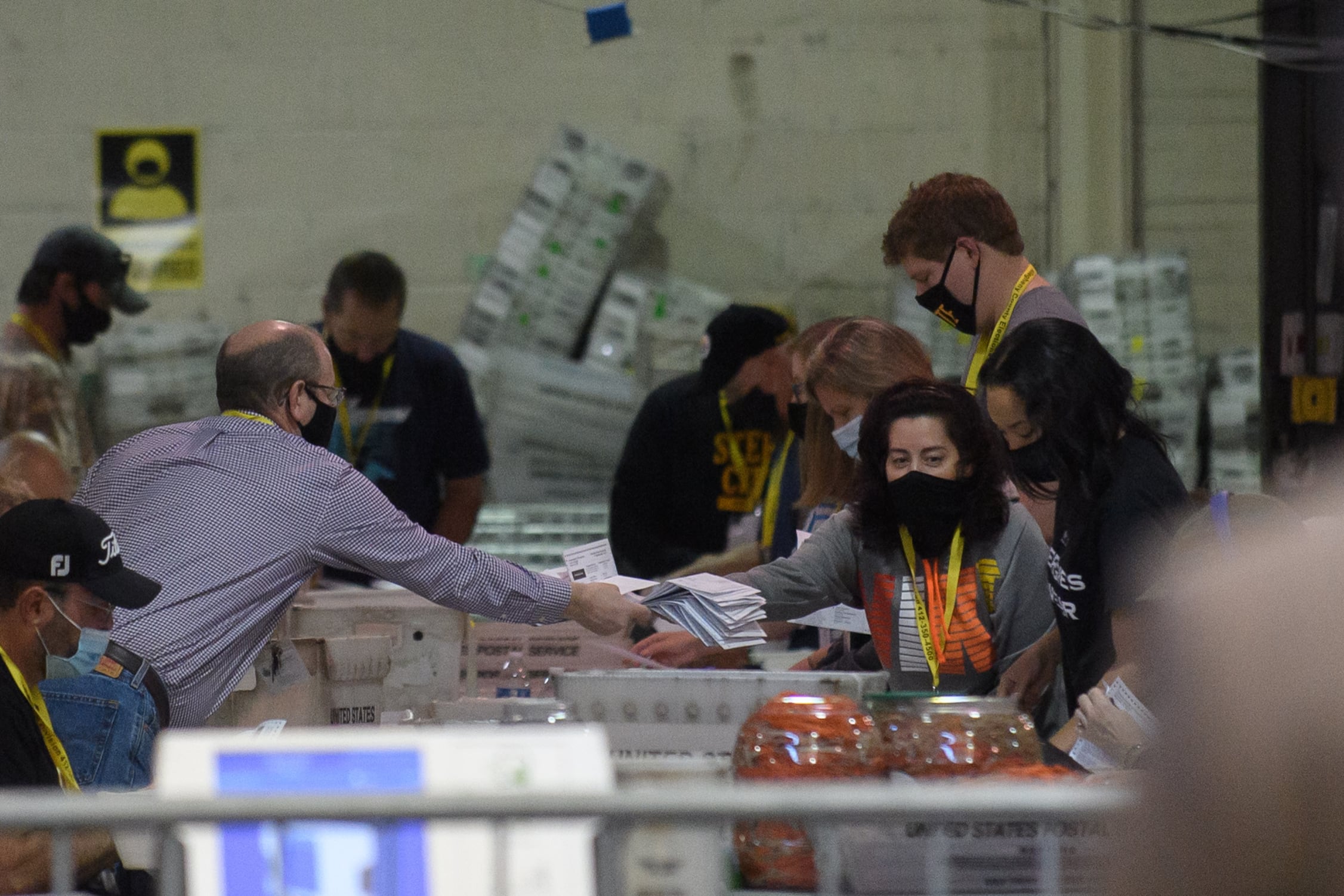 A group of people reach over a large, cluttered table, passing ballots to each other.