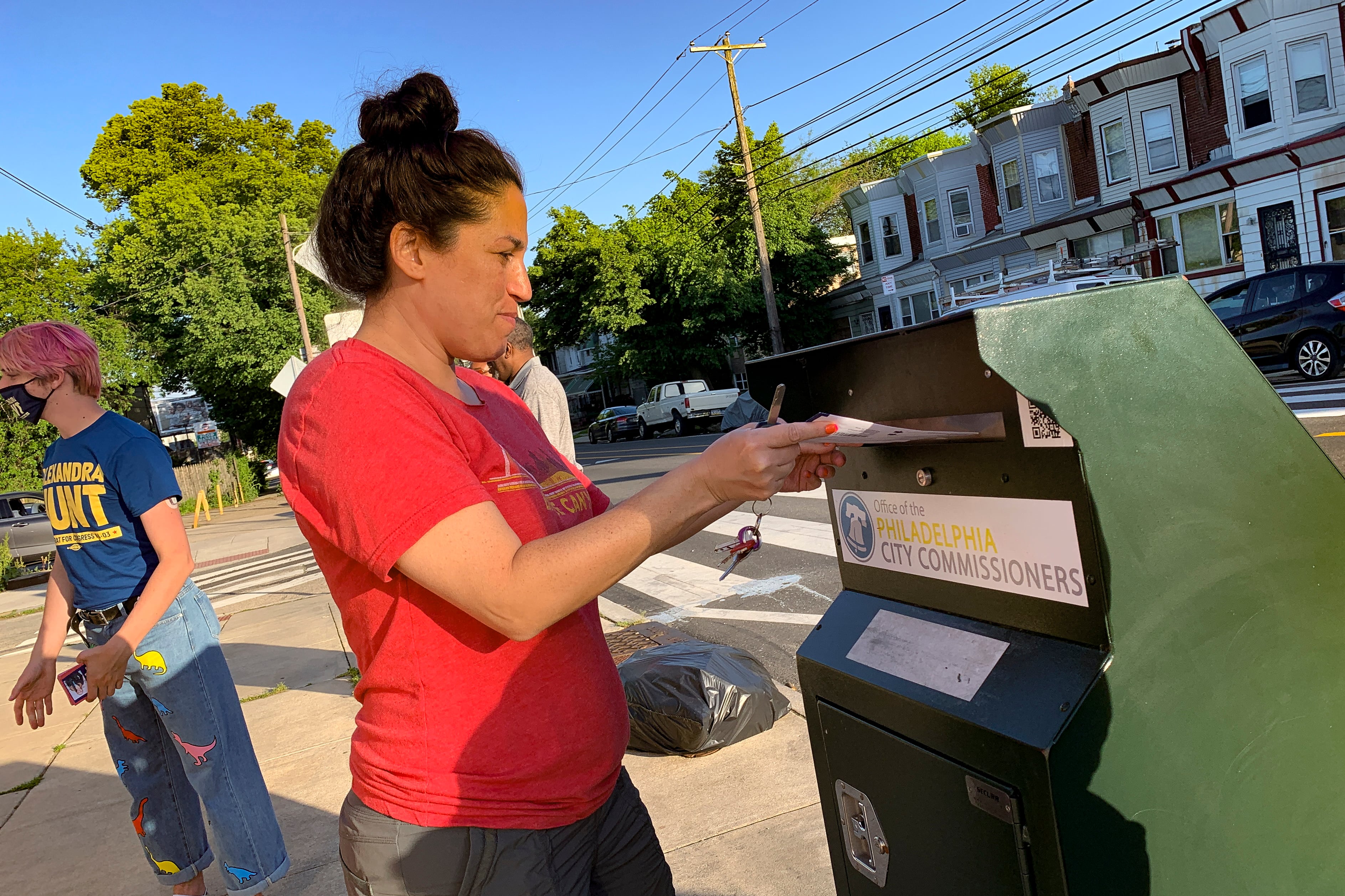 A voter drops a ballot in a green drop box in on the street in Philadelphia.