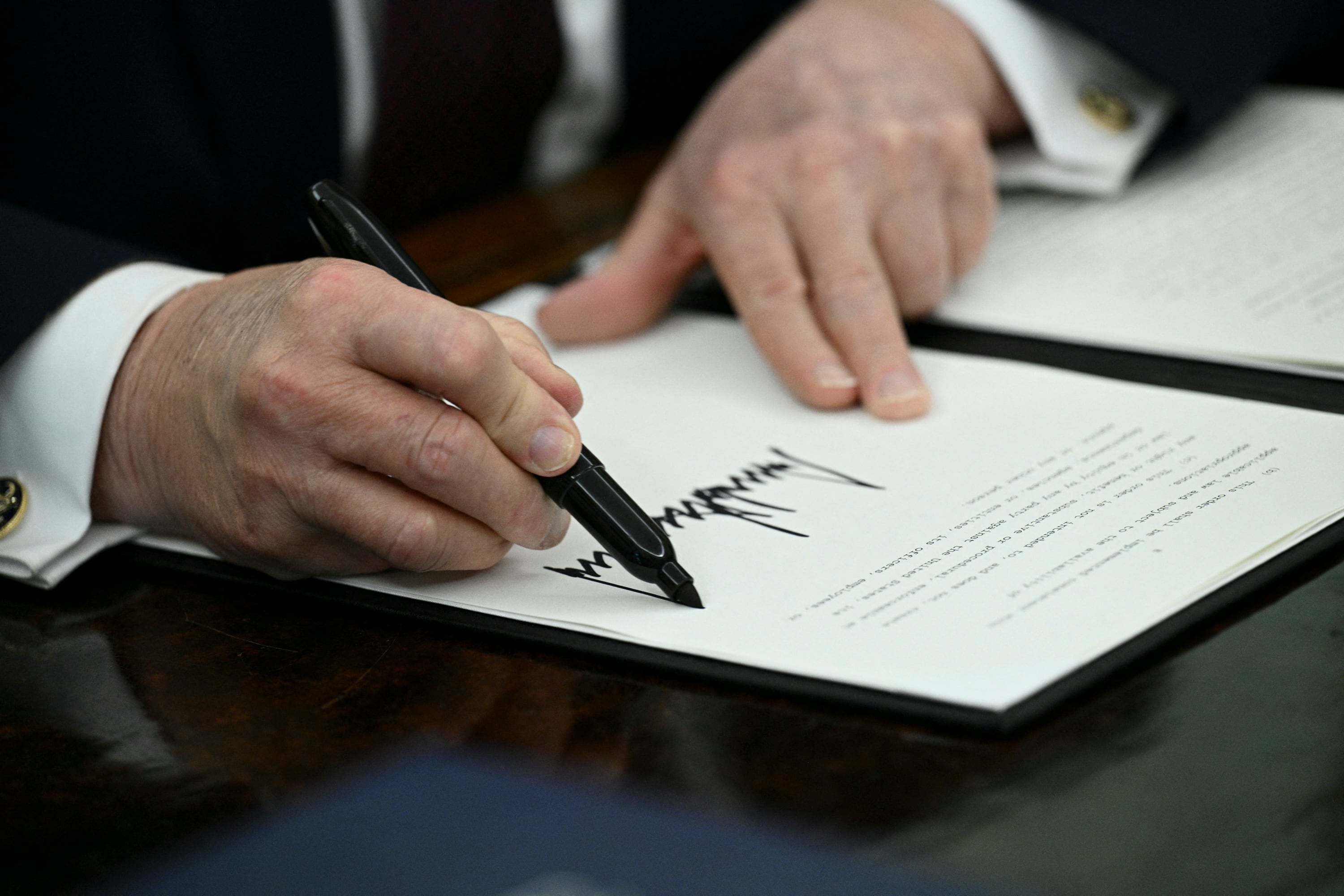 A pair of hands holding a pen and signing on a document.
