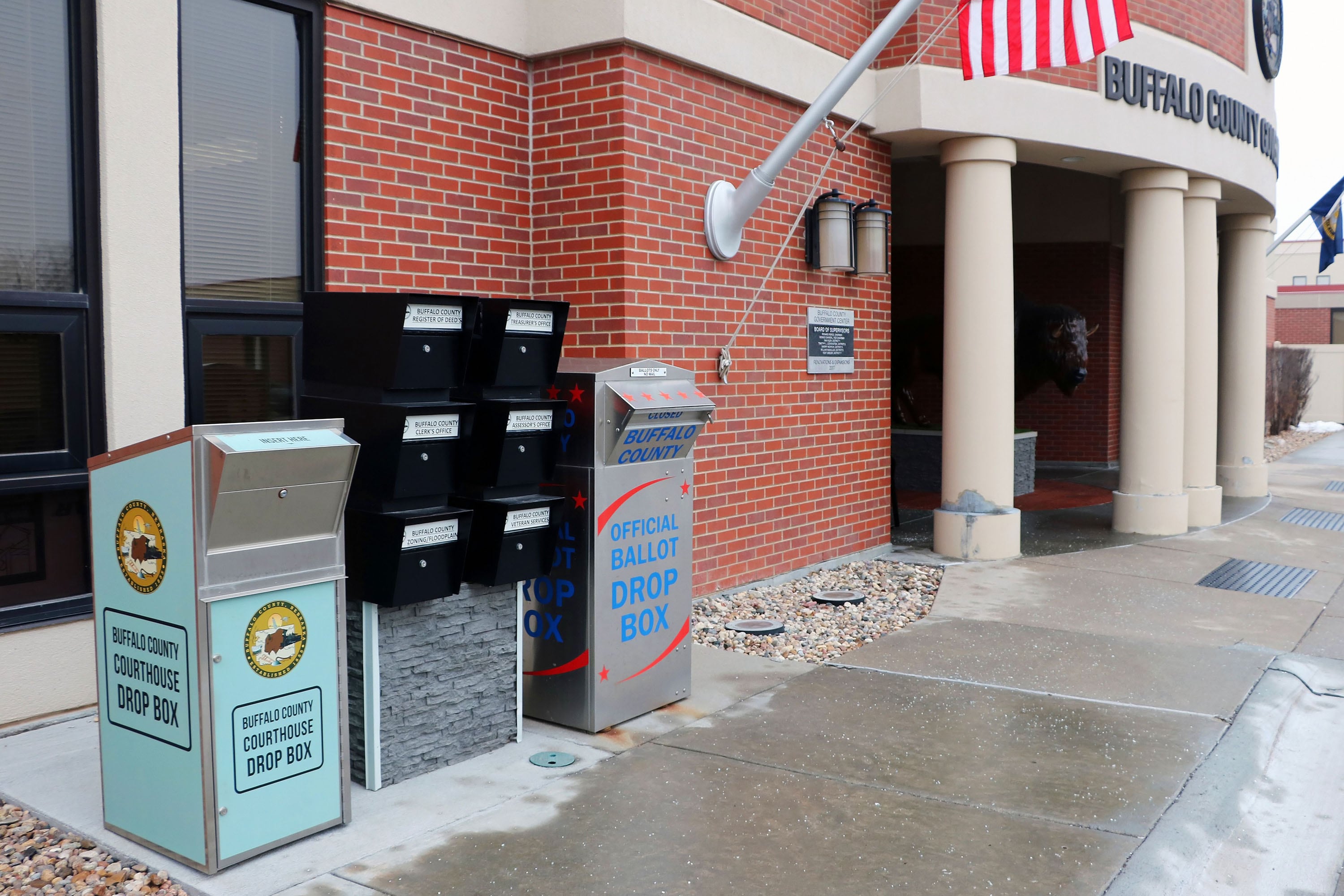 Ballot drop boxes outside of a large brick building county courthouse on a cloudy day.