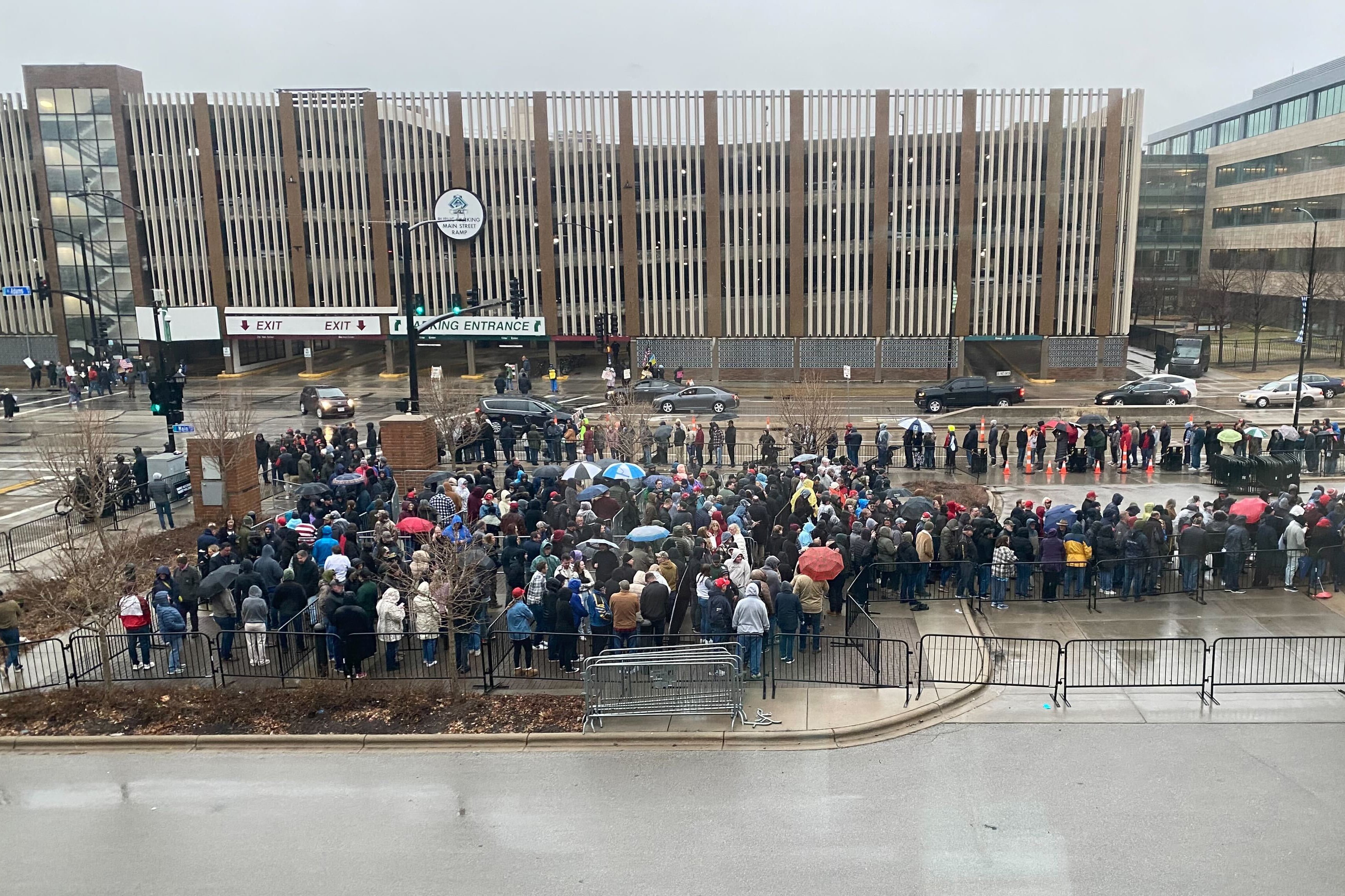 A large crowd of people stand outside on a rainy, cloudy day in front of a building.