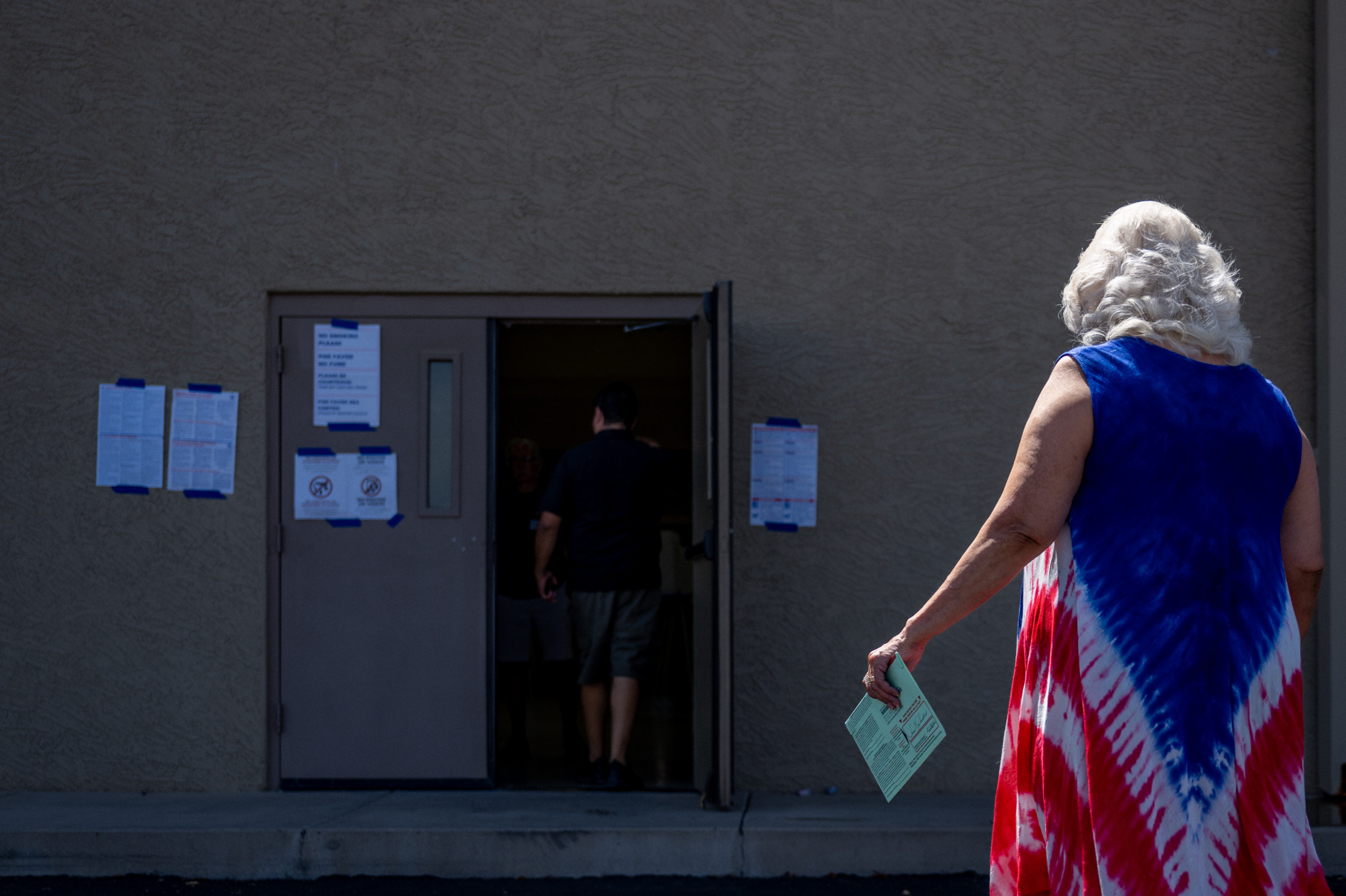 A woman in a red, white, and blue dress approaches an open door.