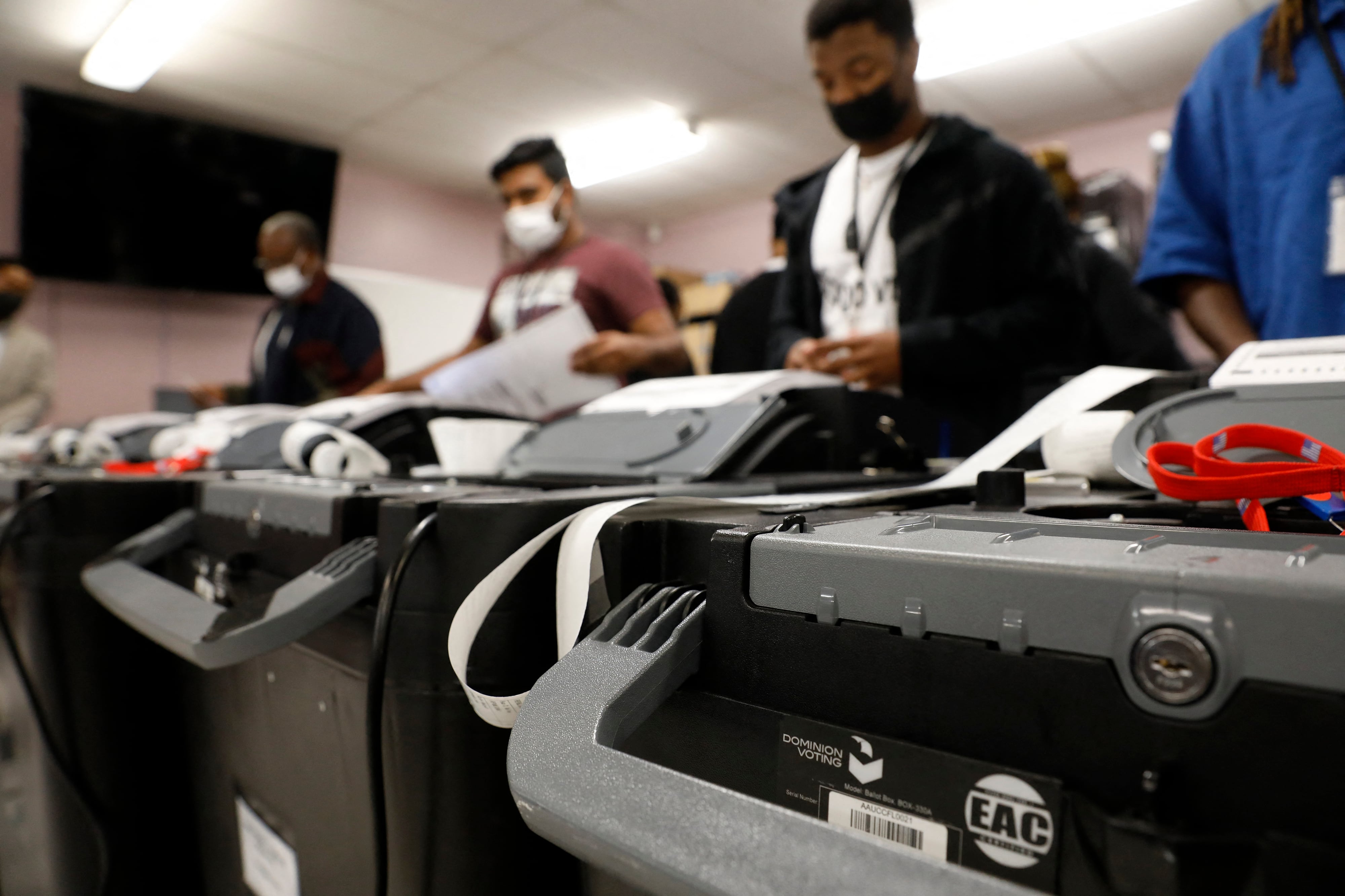 People stand behind a few voting machines.
