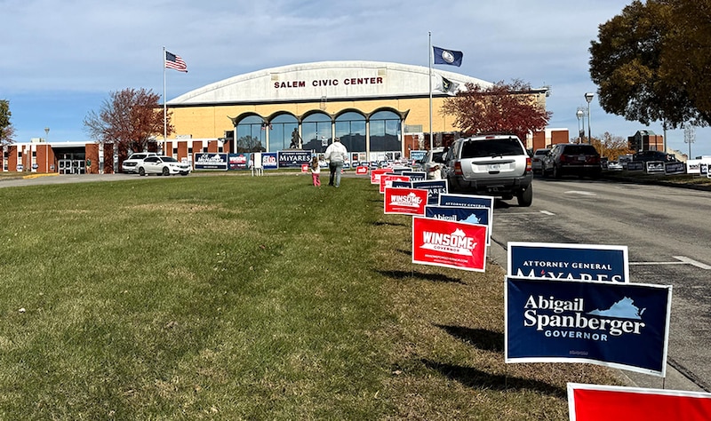 Election signs sit outside a yeallow-and-white building.