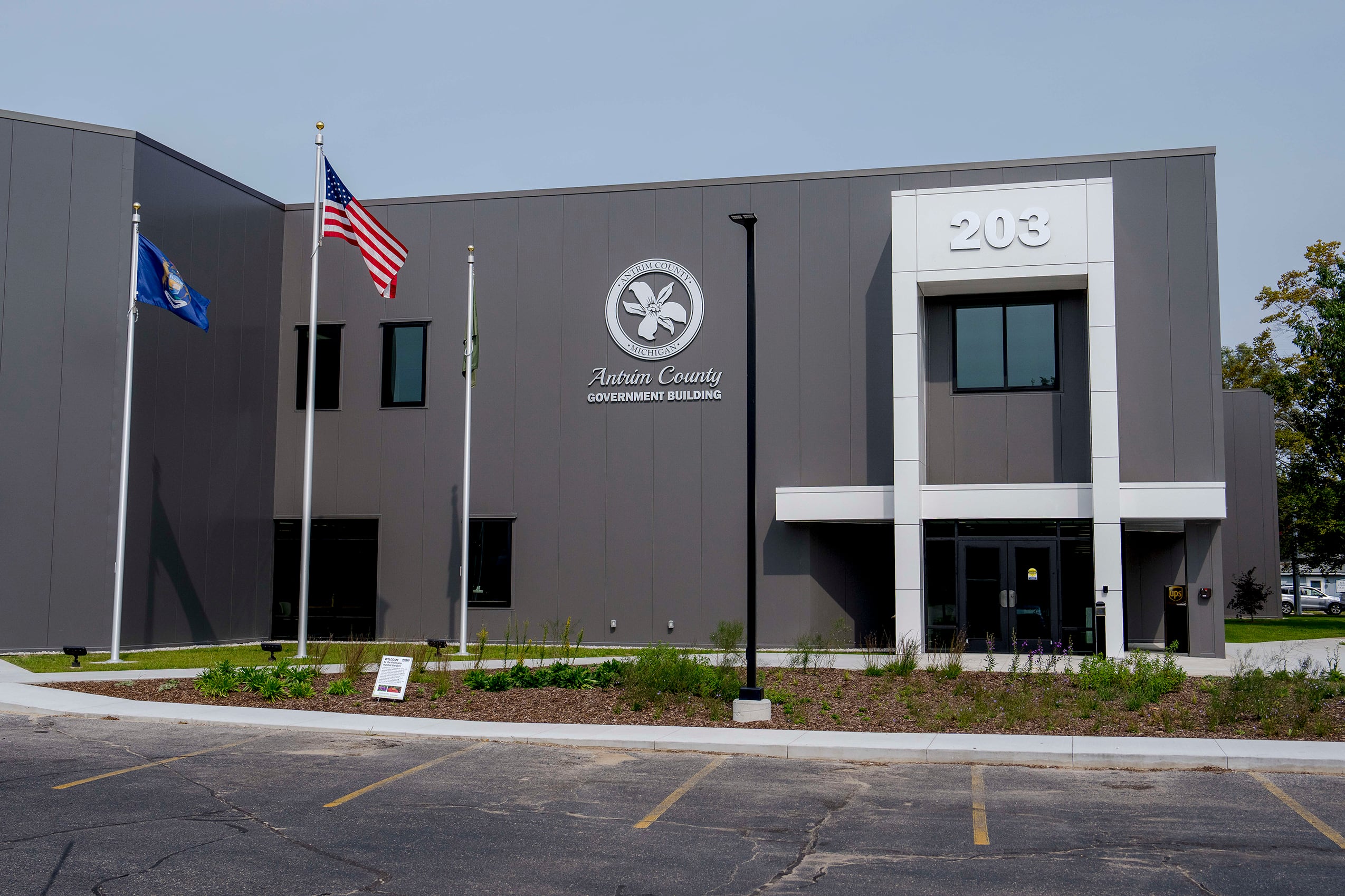 A photograph of a grey building with two flags out front on a sunny day.