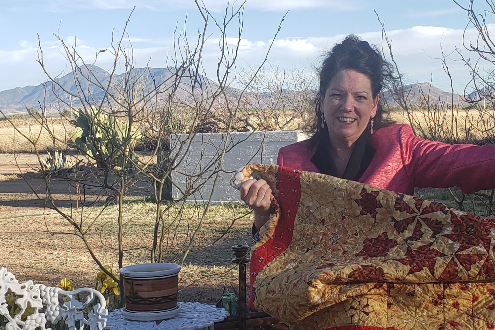 A woman seated outside holding a quilt with mountains in the background