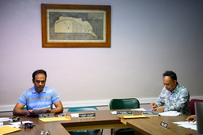 Two men sit at opposite sides of a table in a conference room.