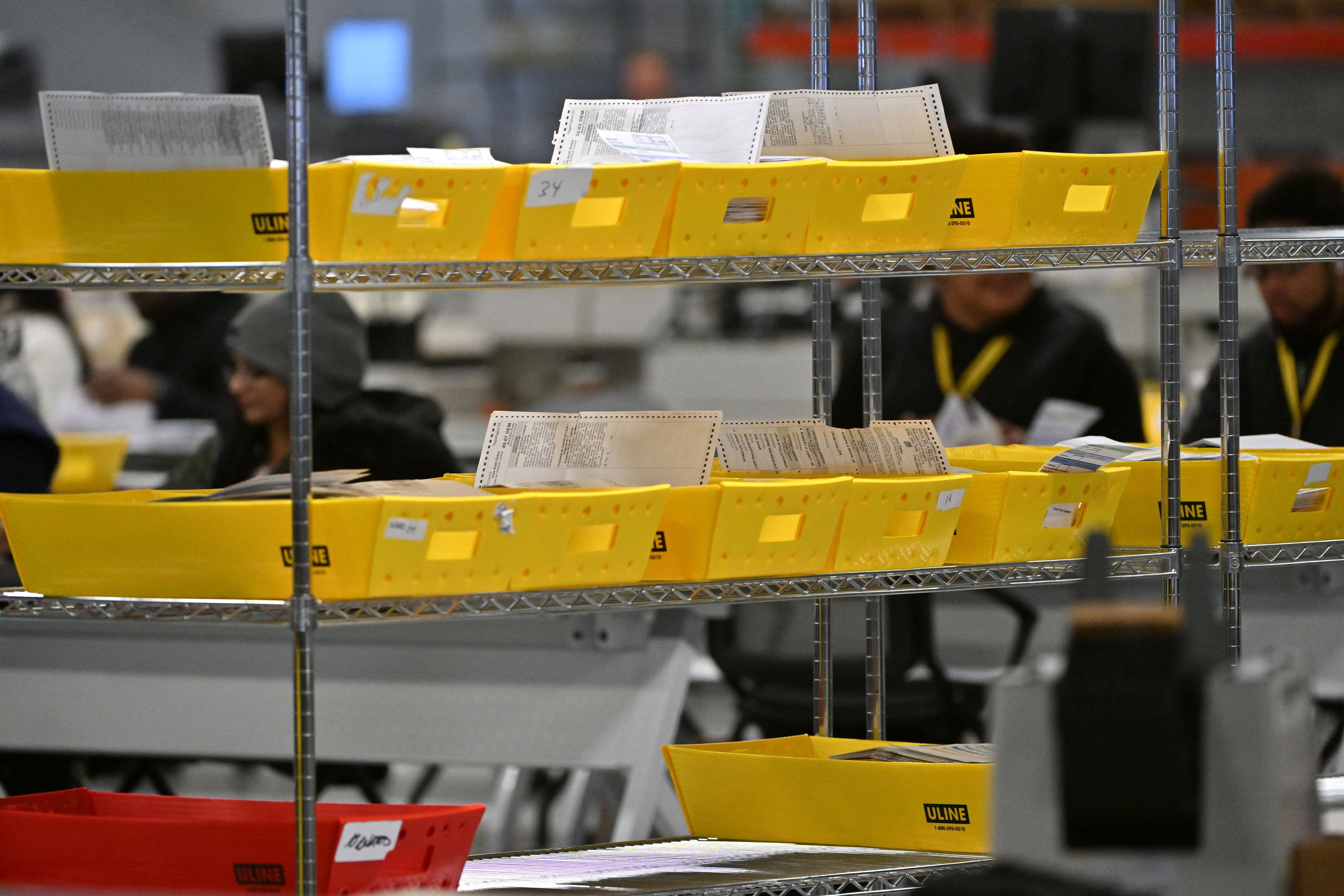A metal rack holding yellow containers with mail-in ballots.