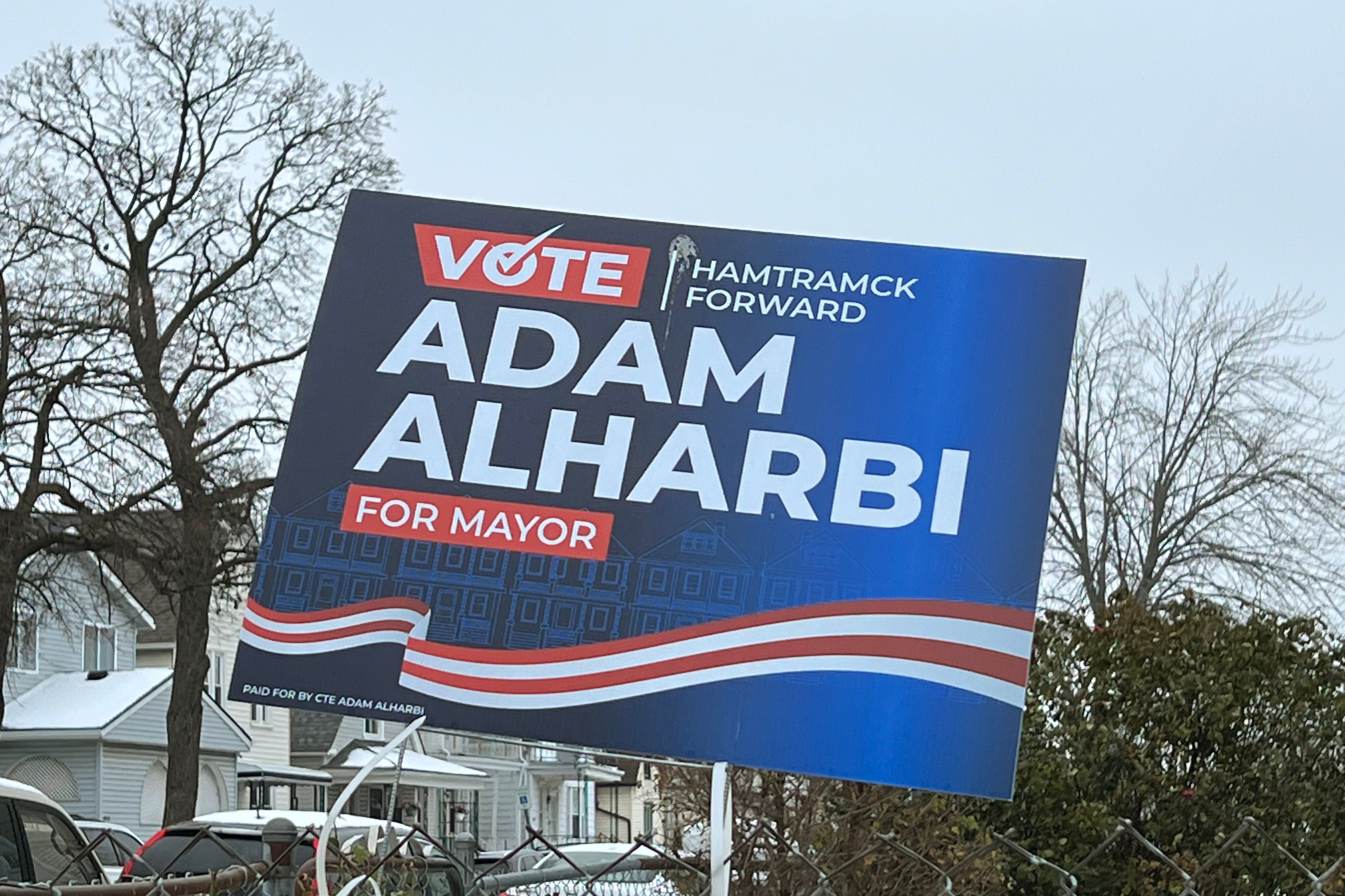 A photograph of a political yard sign outside on a grey winter day.