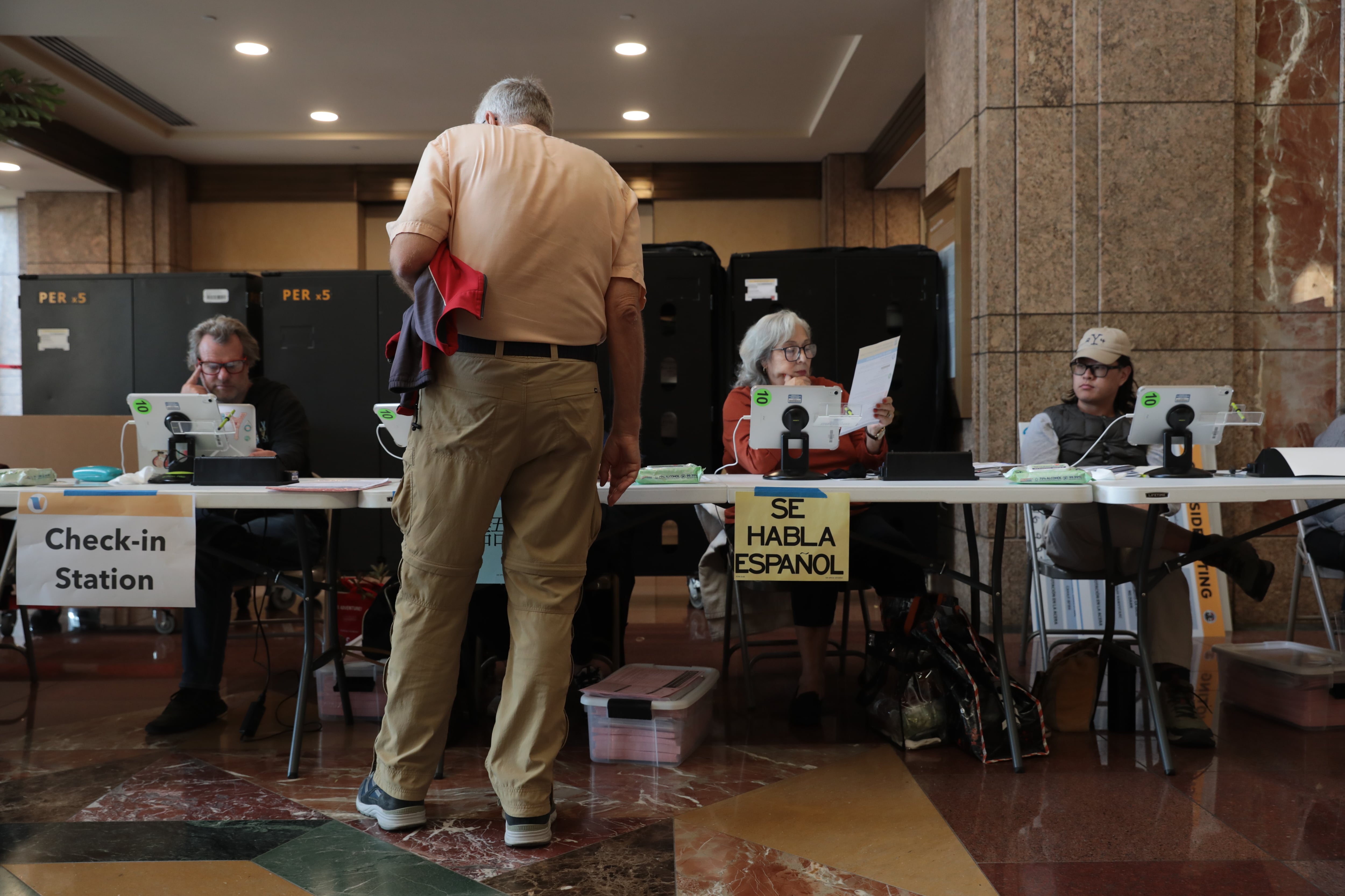 A man in a light shirt and khakis stands at a polling table.
