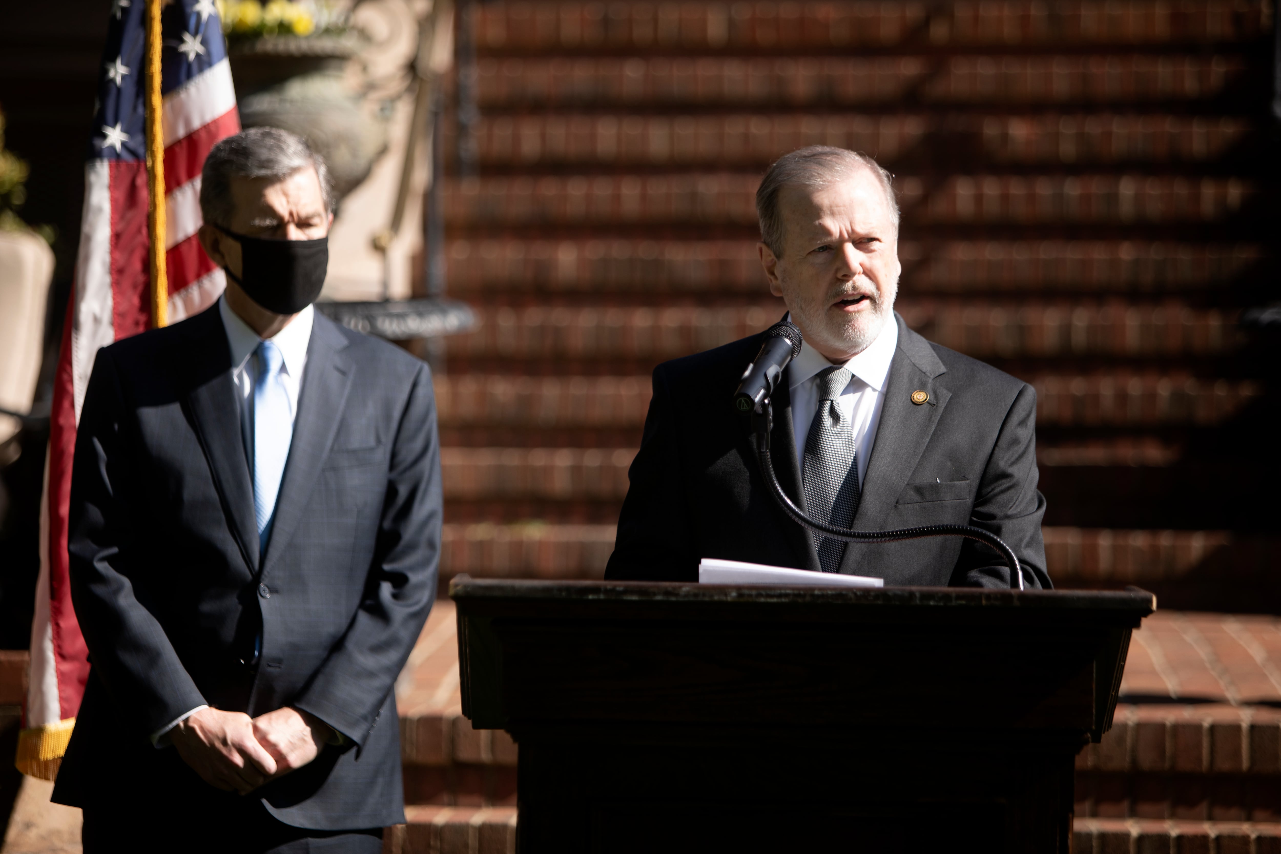 Two men in suits stand in front of steps