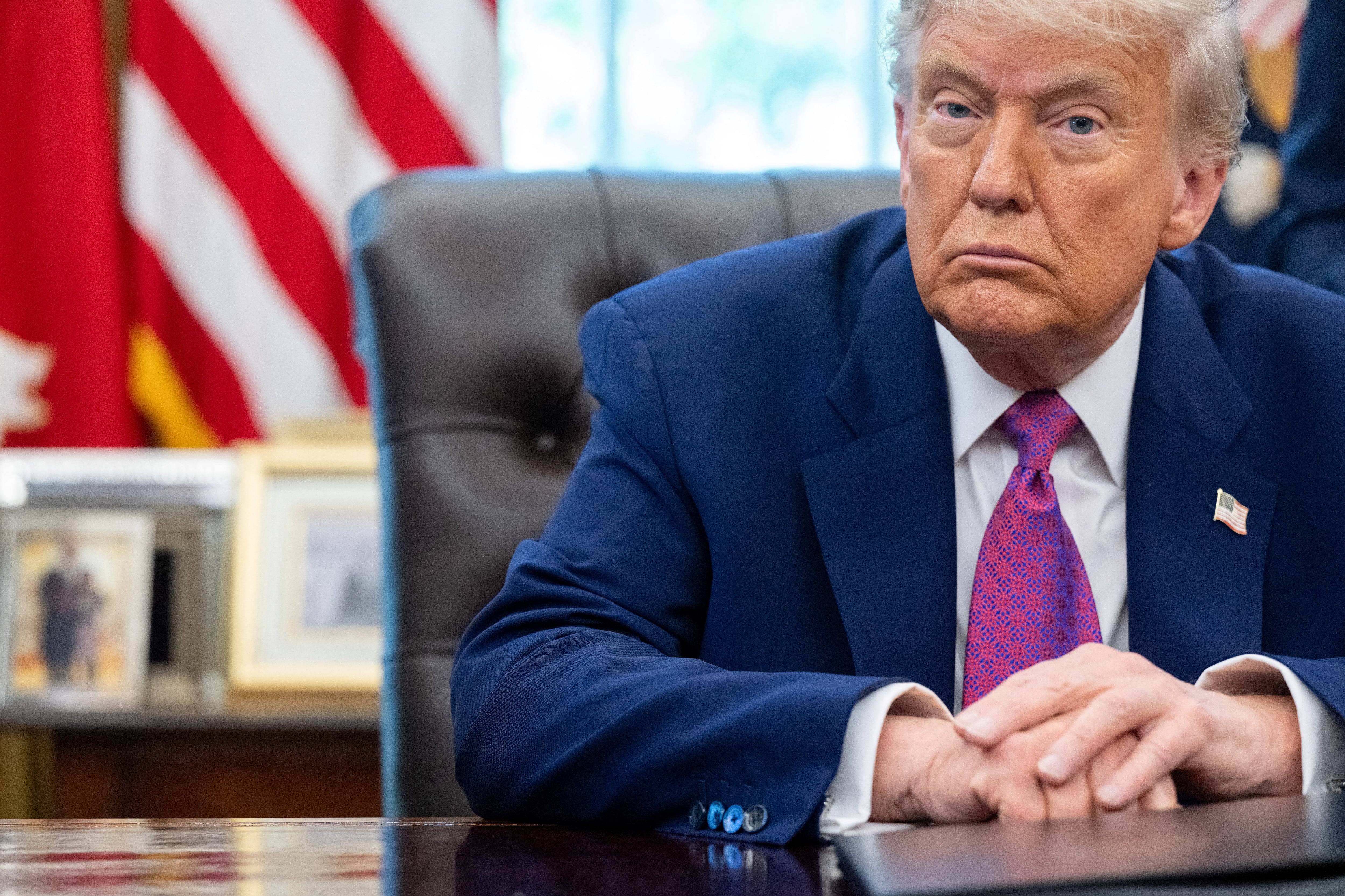 The President in a blue suit and pink tie sits at a desk and looks at the camera.