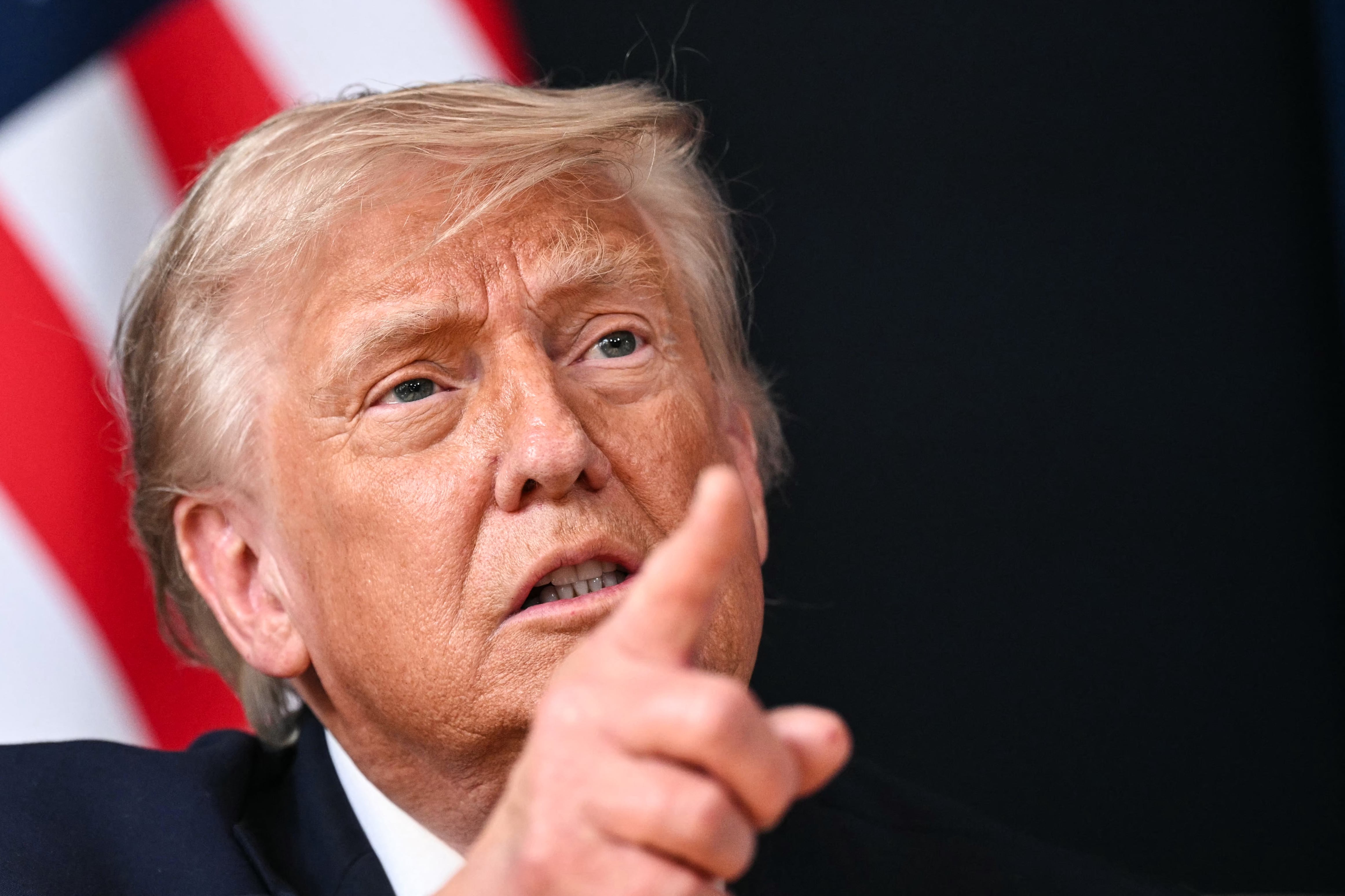 Donald Trump points in front of an American flag.