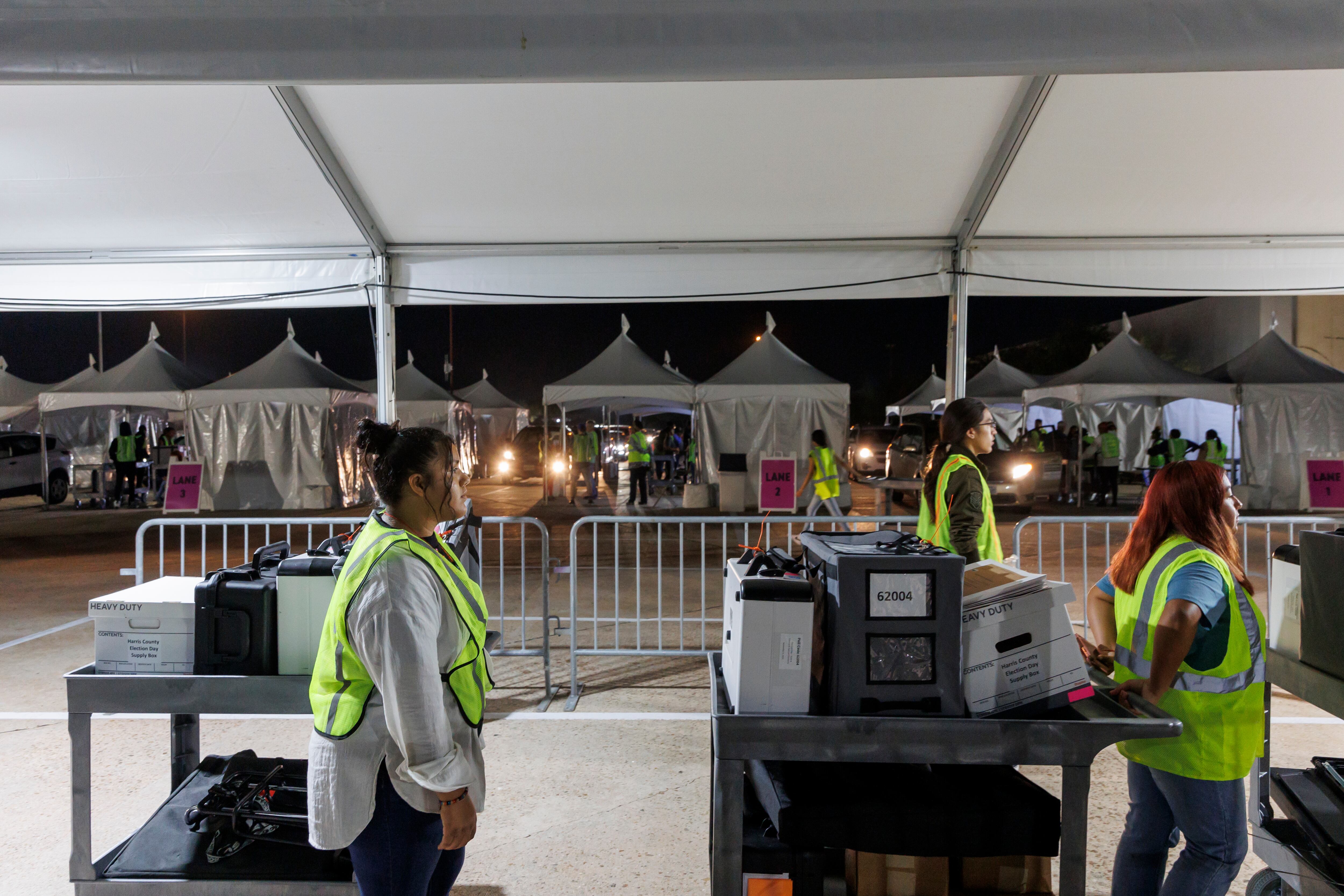 Workers in yellow vests pull carts carrying boxes and machines under a night sky