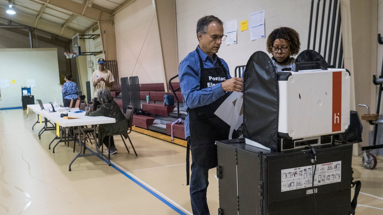 A man and a woman stand in front of a white machine in a gymnasium.