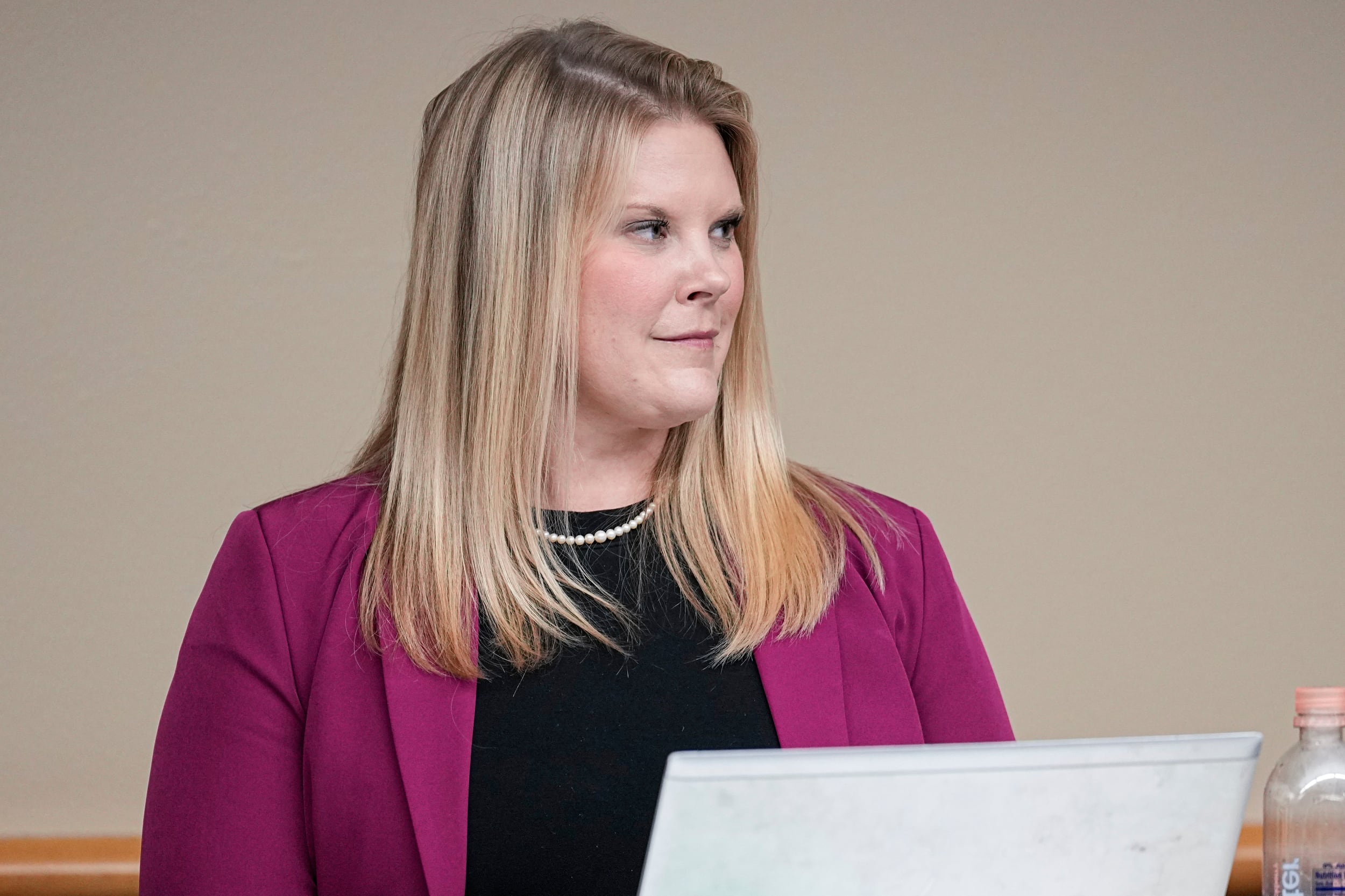 A woman with a magenta jacket and black top looks to her left.