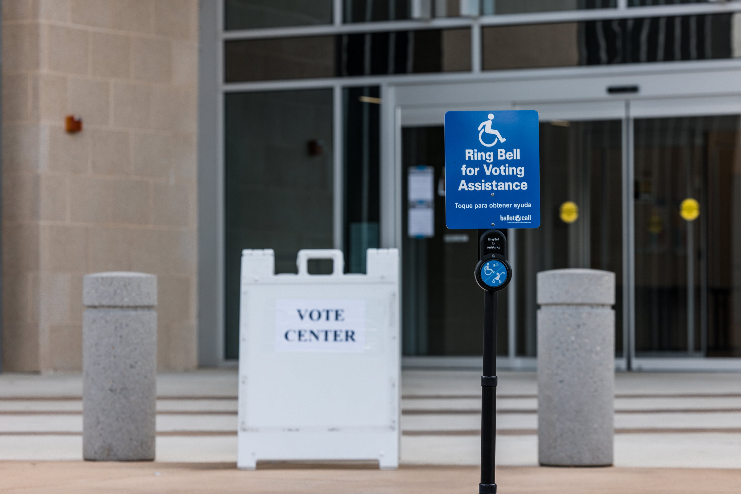 A white sign standing on a side walk next to a handicap parking sign and in front of a building reads " Vote Center" in black letters.