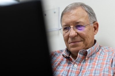 A man wearing glasses and a red, white and blue striped shirt looks at a computer screen.