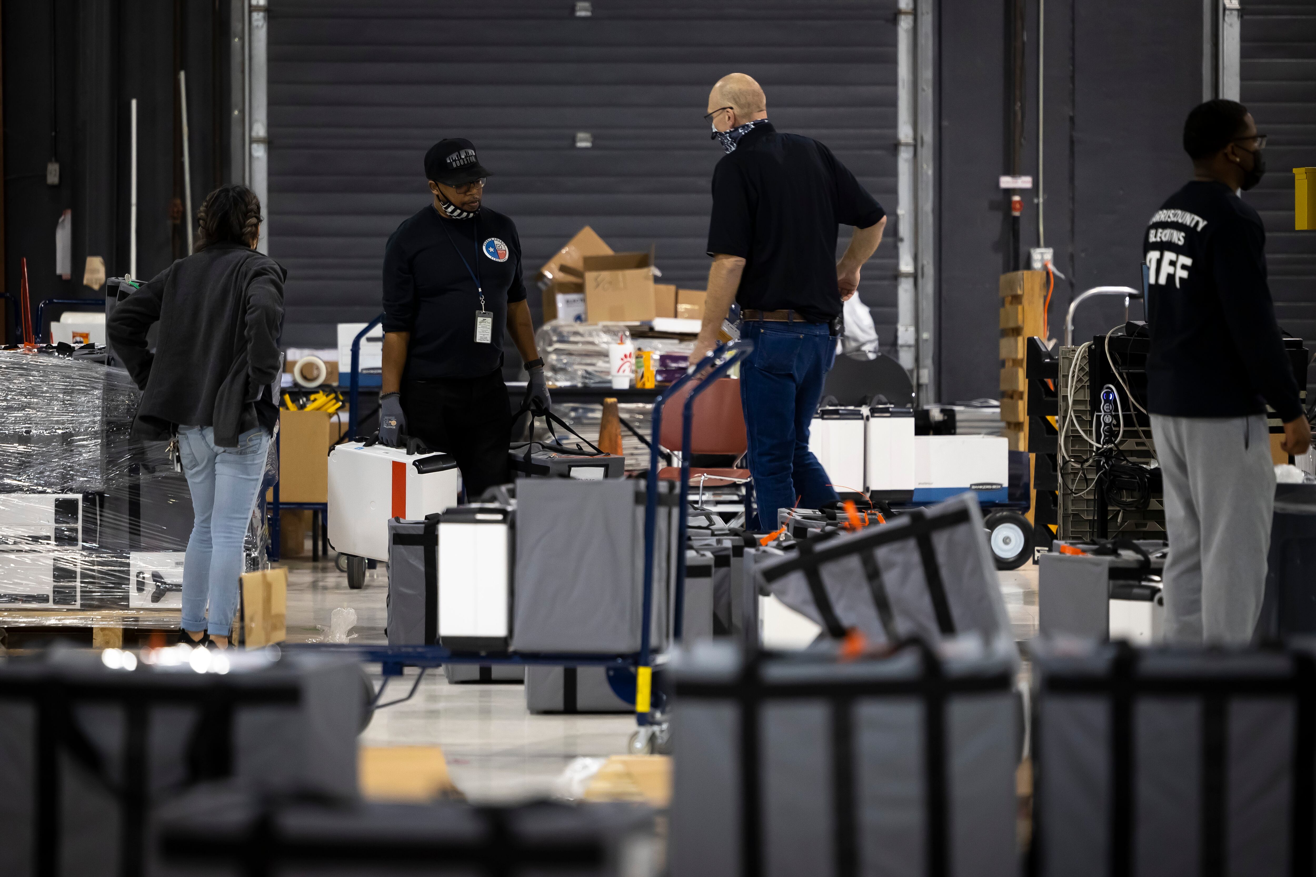 People stand in the middle of a warehouse surrounded by cardboard boxes and storage bags