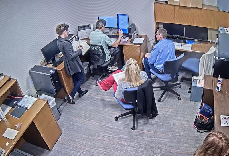 Four people work in a room, three people are sitting and one person is standing.