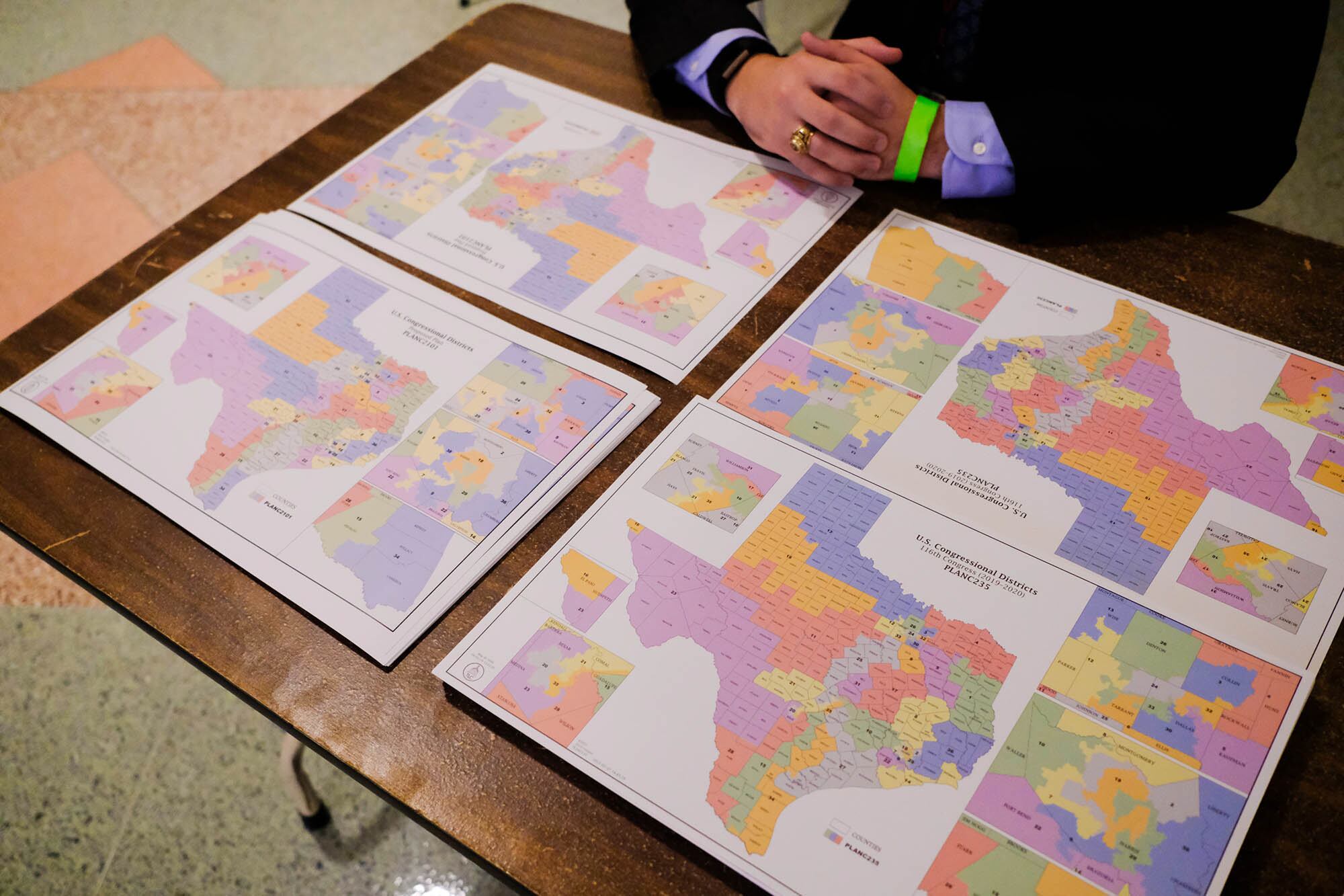 A view of four different maps of Texas and a pair of hands on a desk.