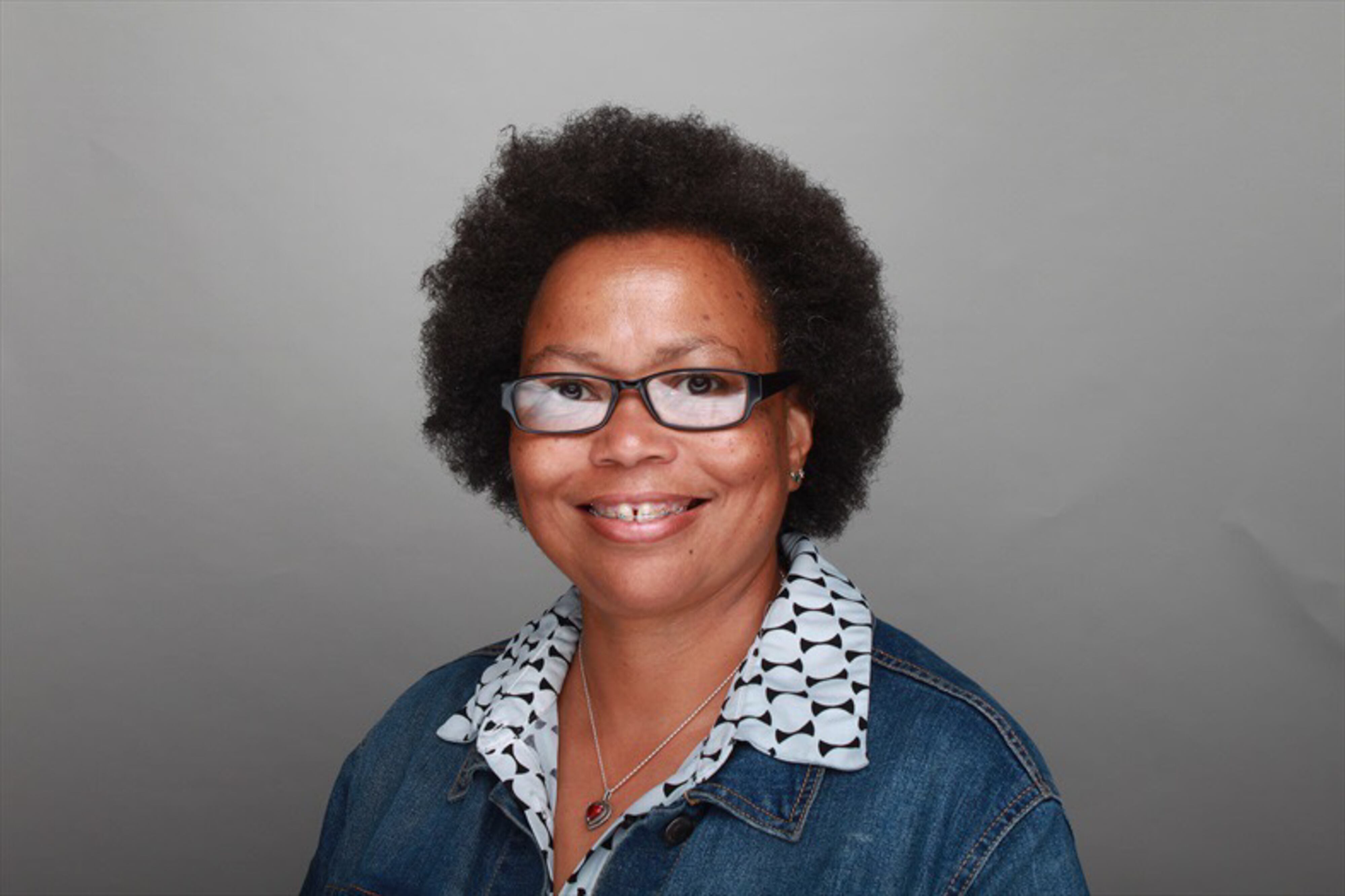 A dark-haired woman smiles as she poses for a photographic portrait against a gray background.