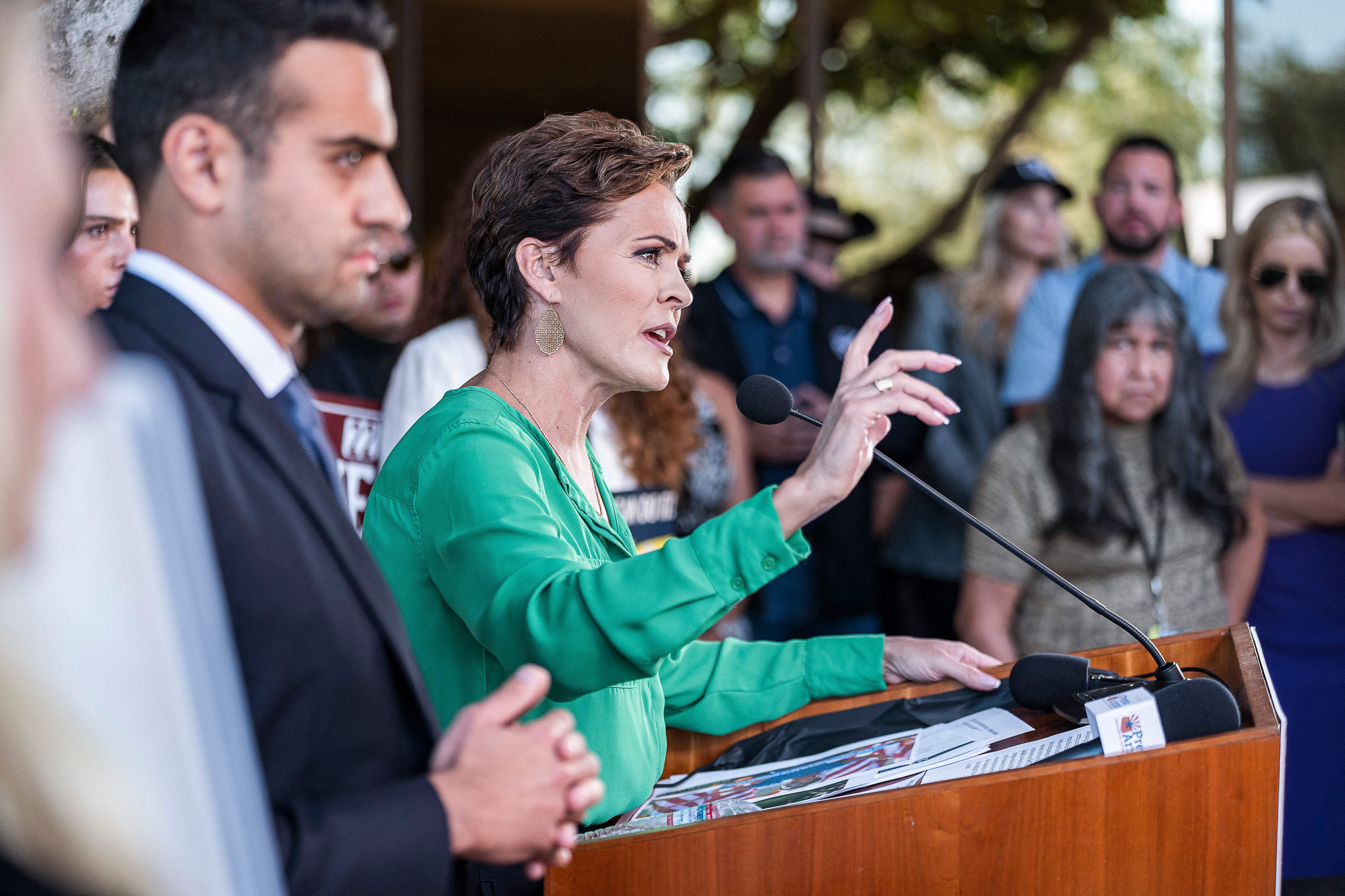 A woman speaks from a lectern while a man standing beside her looks out into a crowd 