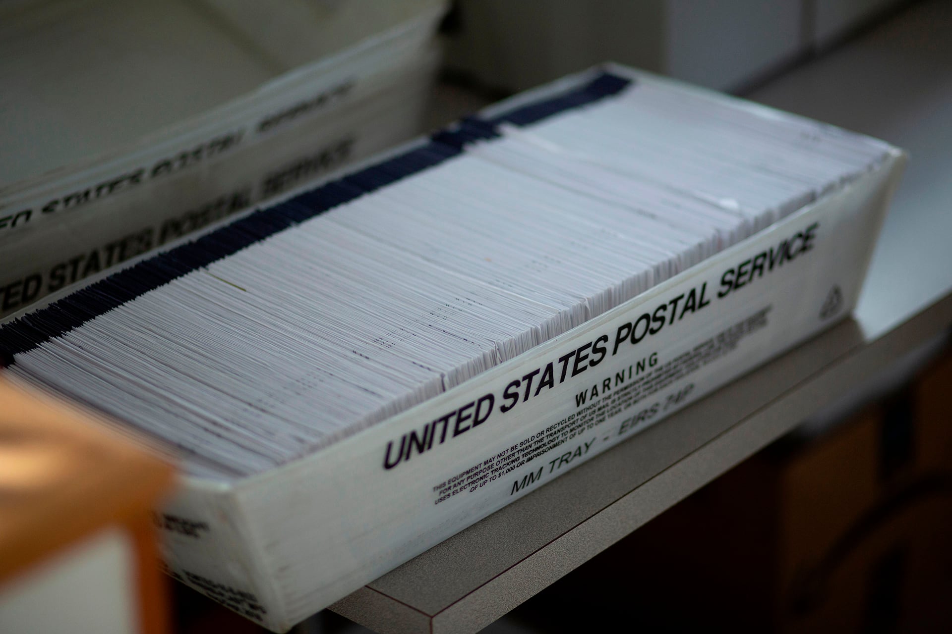 A white box with black words that say, "United States Postal Service", is full of election ballots.