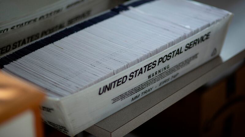 A white box with black words that say, "United States Postal Service", is full of election ballots.