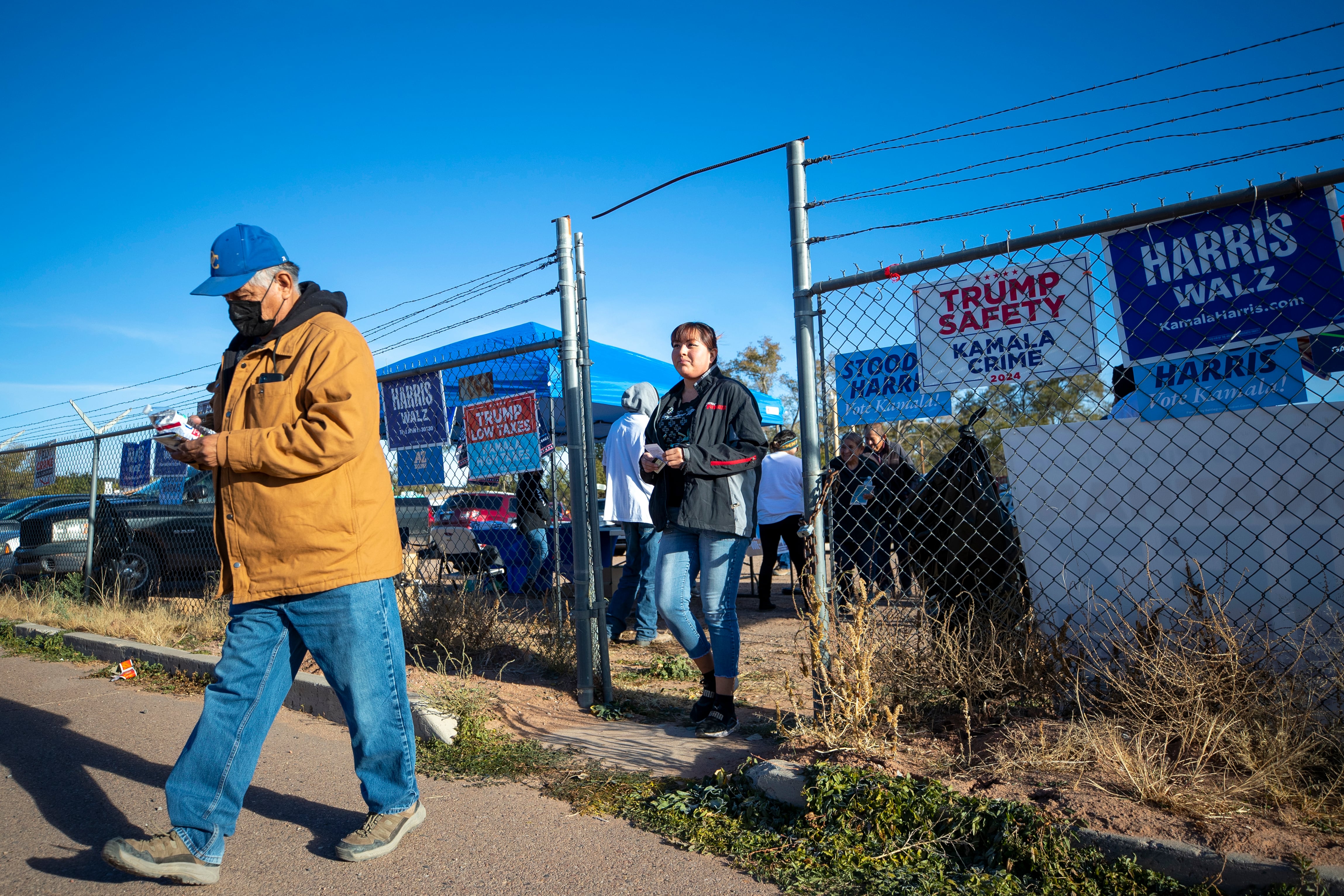 Two people walk under a barbed wire fence with political campaign signs lining the side outside.
