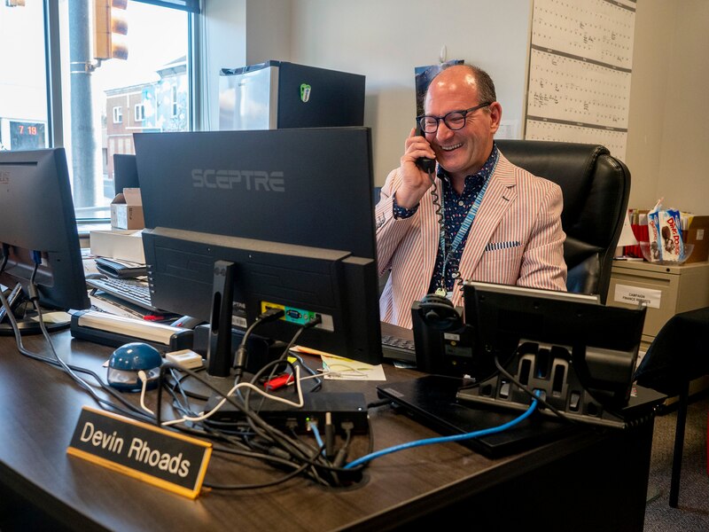 a man wearing a red and white striped suit answers the phone while sitting at a desk behind a computer screen.