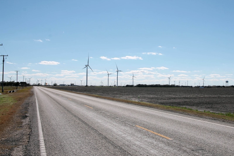 An empty highway with wind turbines on both sides and a blue sky.