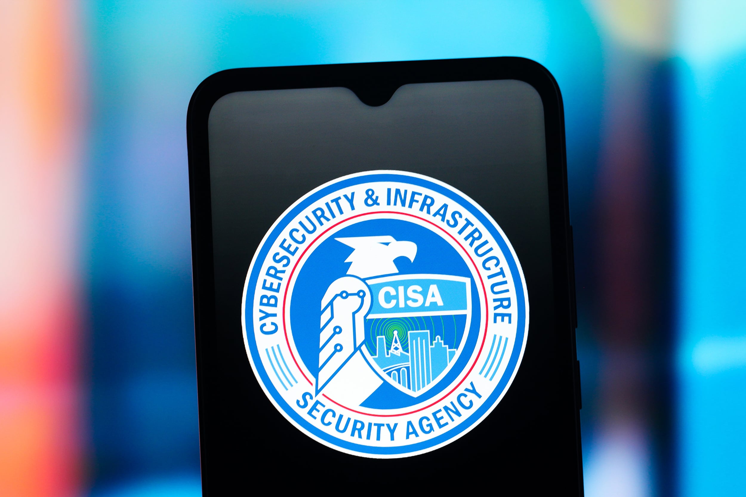 In this photo illustration, the United States Cybersecurity & Infrastructure Security Agency logo is seen on a cellphone screen with a colorful blurred background.