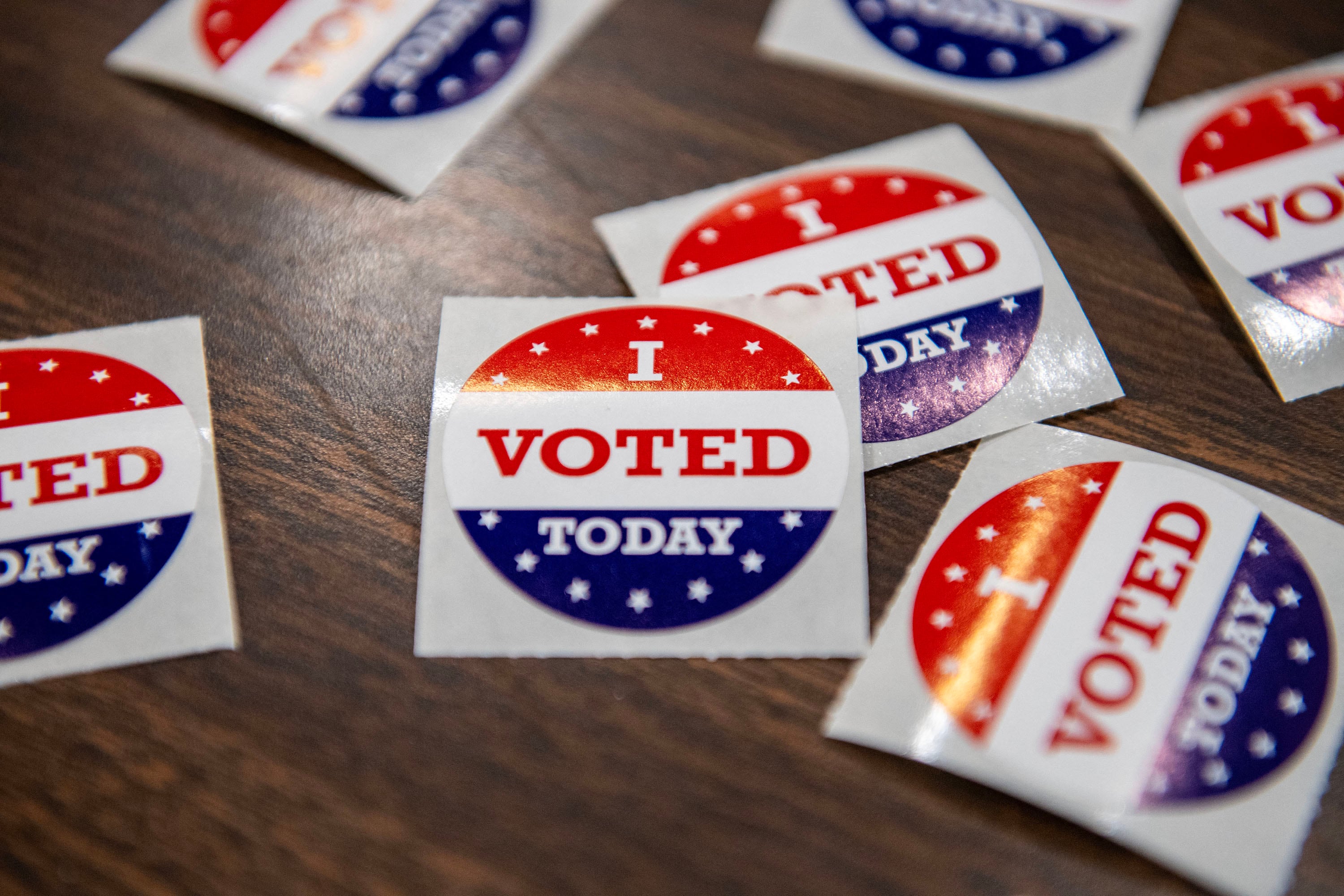Round, white, blue and red stickers that read "I Voted Today" are spread across a wooden table.