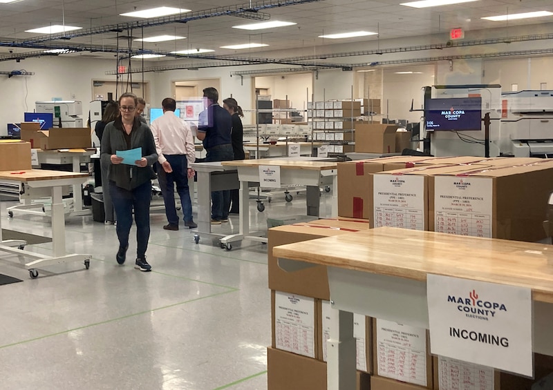 People work in the background of a room full of large cardboard boxes and sorting tables.