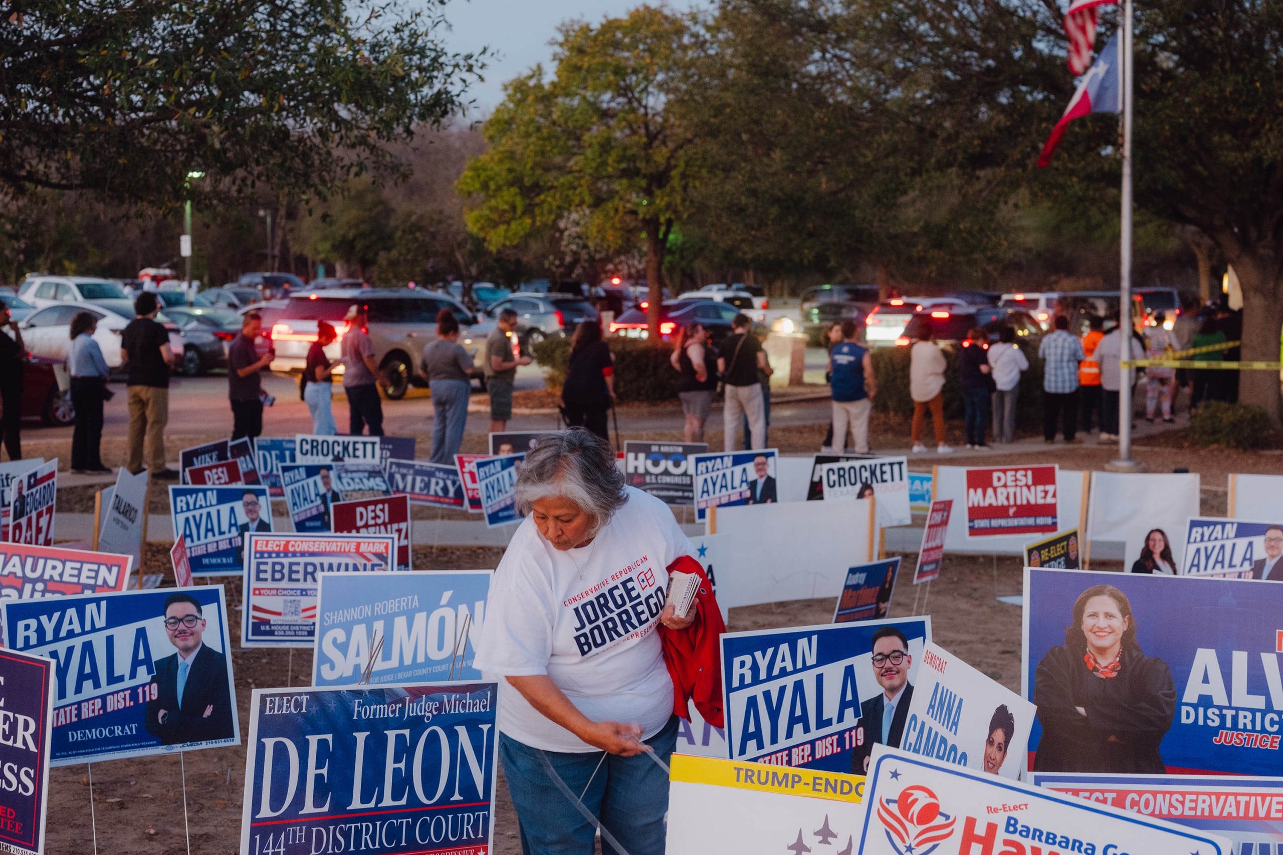 A person stands in a lot of political signs while a long line of people stand in the background.