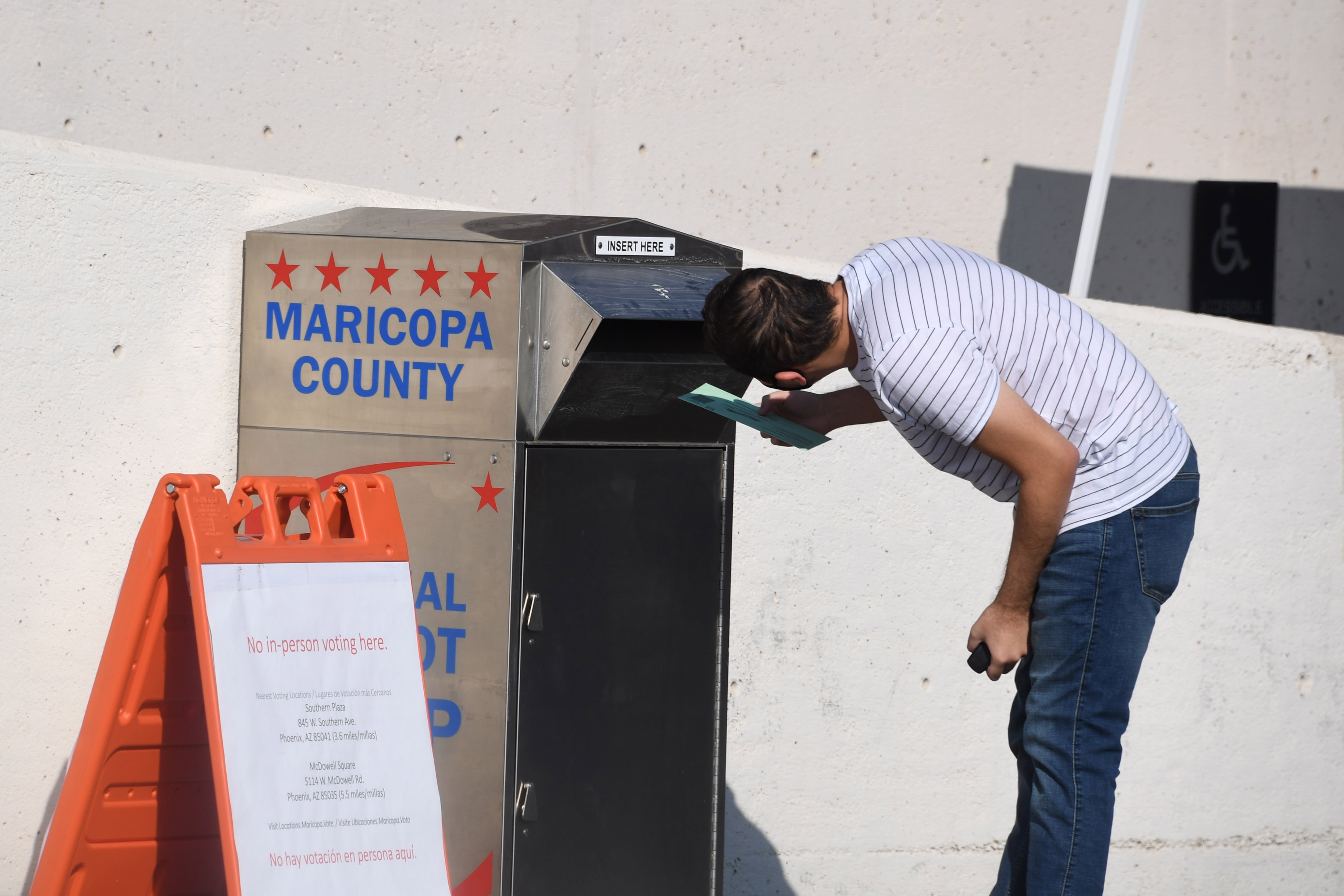 A man bends down to look into the opening of a silver drop box on a sidewalk